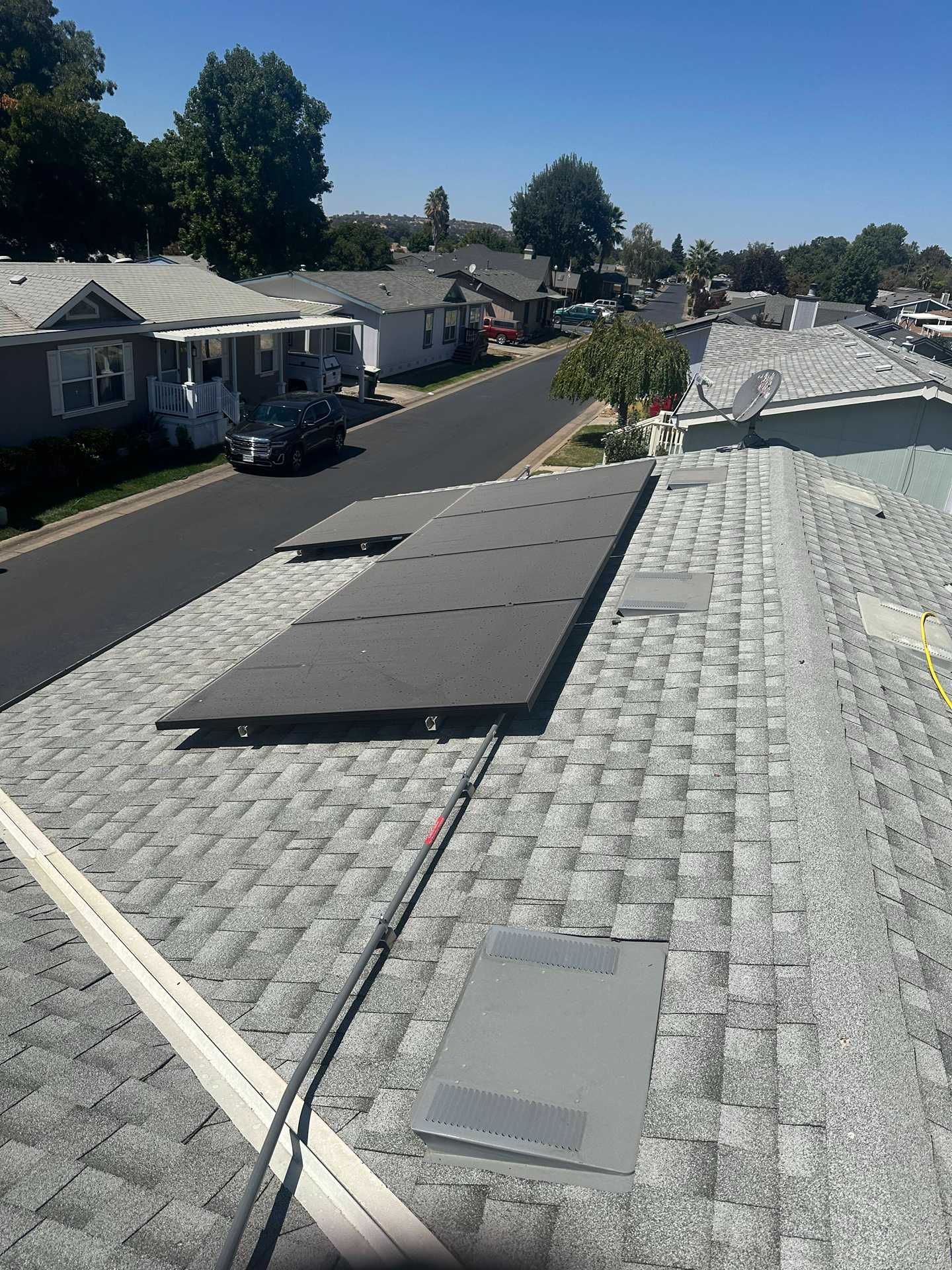 Rooftop with black solar panels overlooking a quiet suburban street and houses