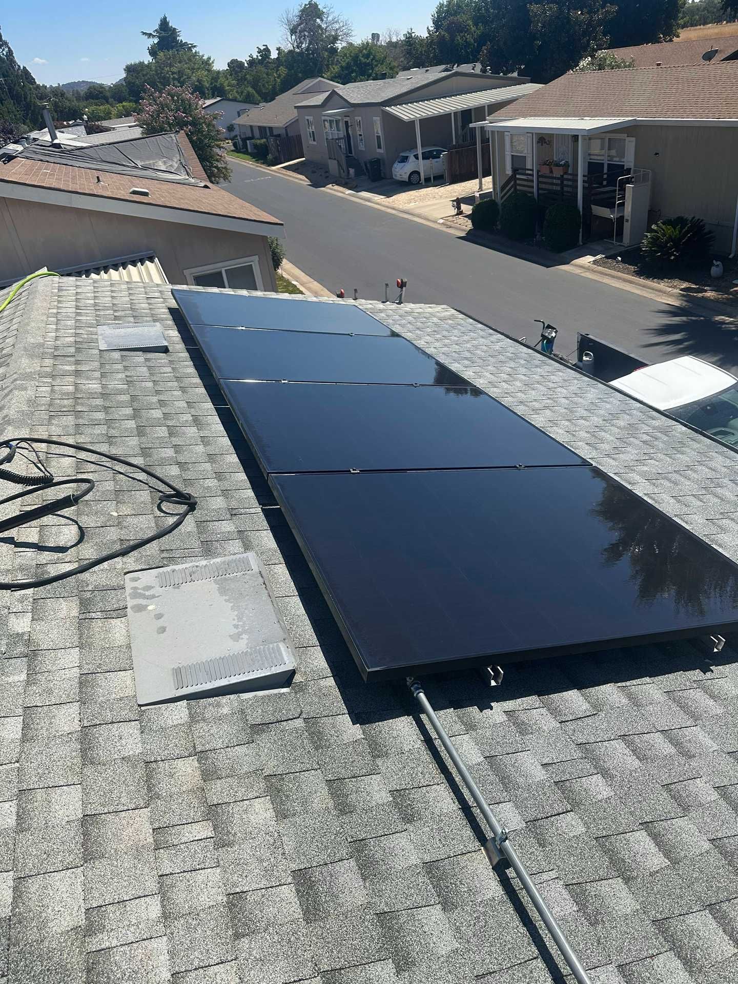 Black solar panels installed on a shingled rooftop in a suburban neighborhood.