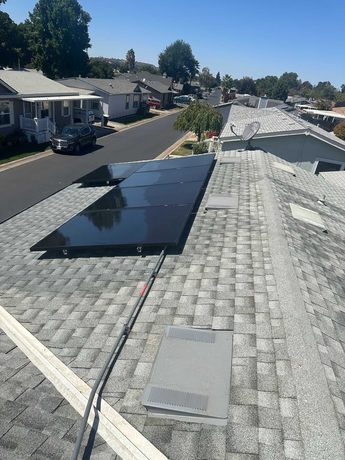 Solar panels on a shingled rooftop in a suburban neighborhood under a clear sky