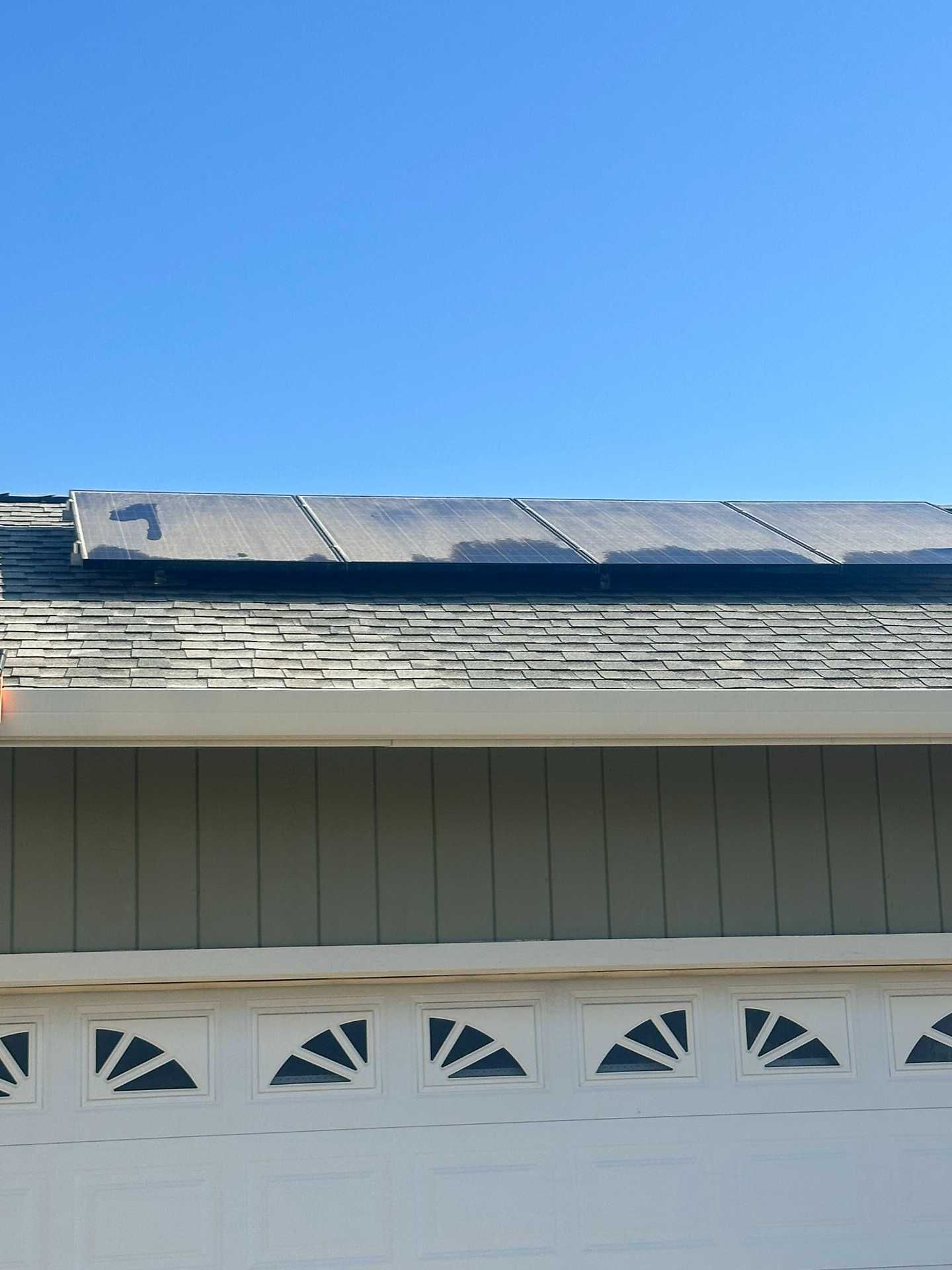 Residential roof with solar panels above a white garage under a clear blue sky