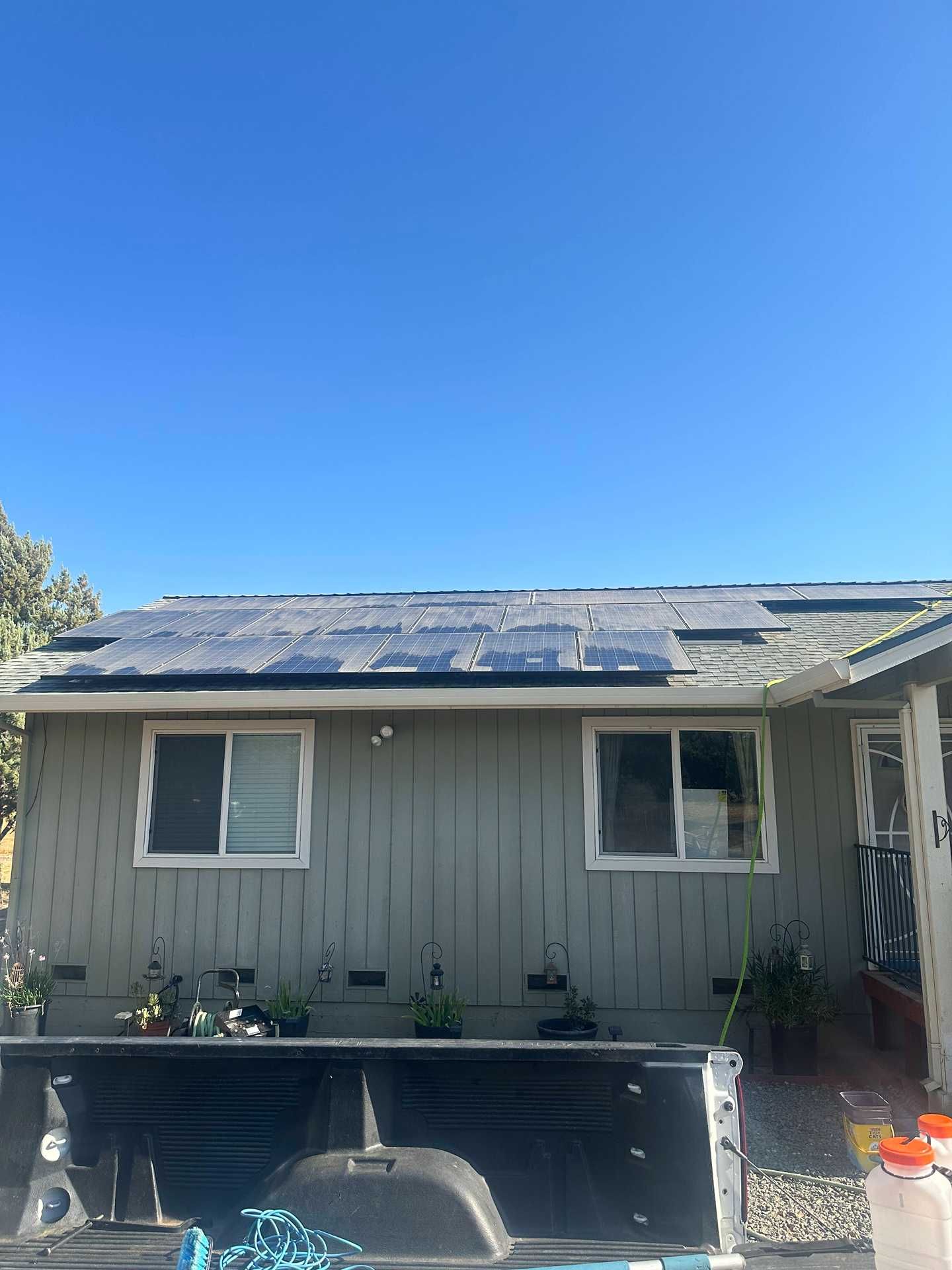 Back of a gray house with solar panels, two windows, and a sunny blue sky