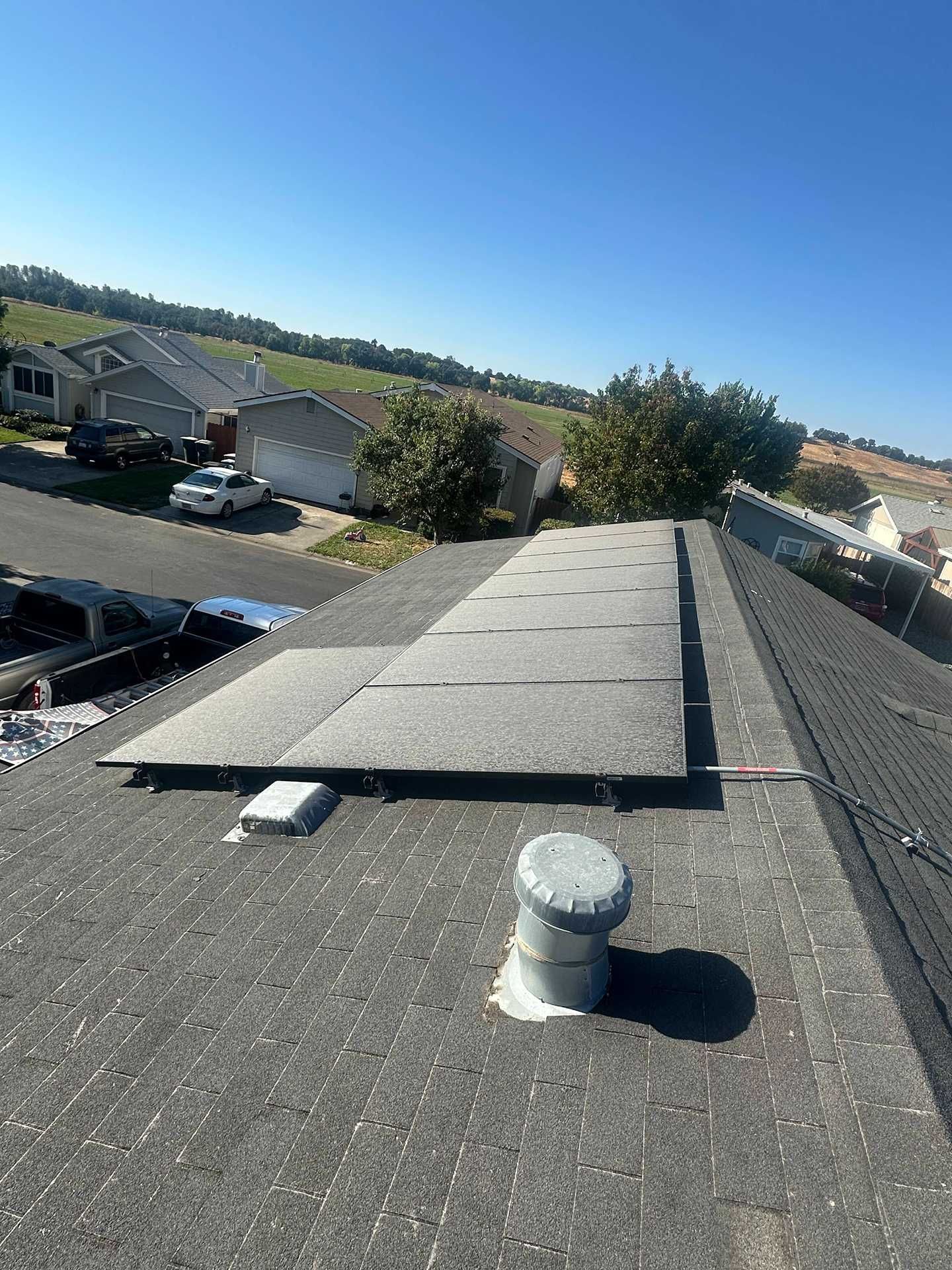 Rooftop with dark shingles, a vent pipe, and a raised black panel under a clear blue sky.