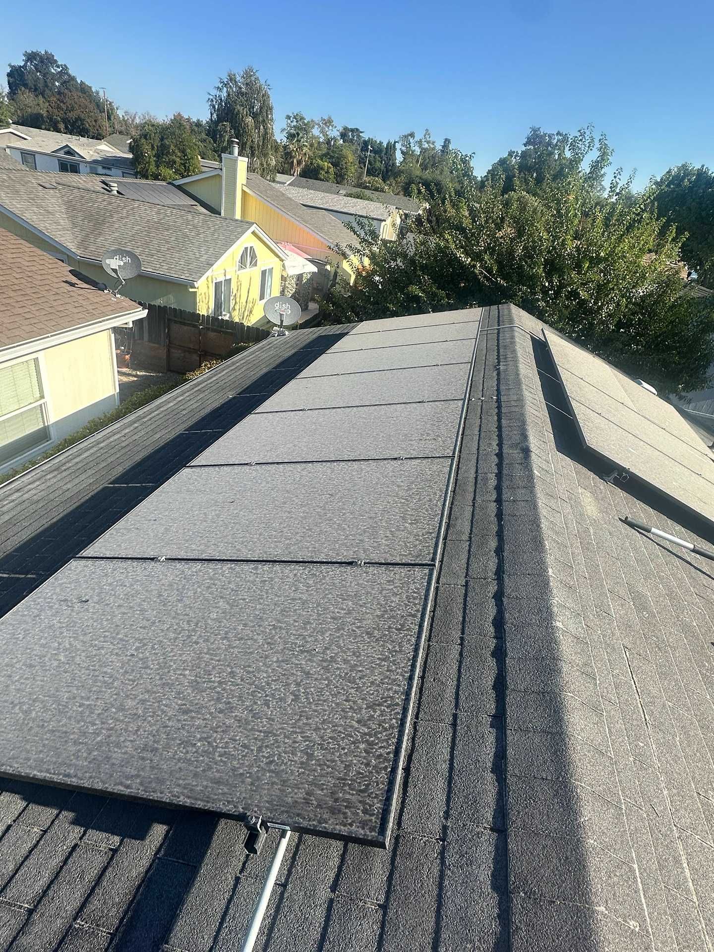 Roof shingles on a house with a tree-lined neighborhood in the background under a clear sky