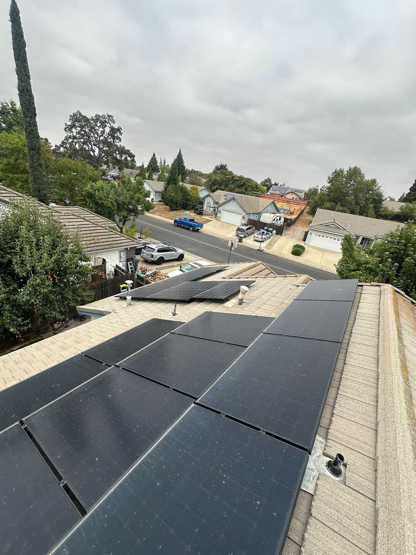 Solar panels on a residential rooftop under a cloudy sky, with a neighborhood street in the background.