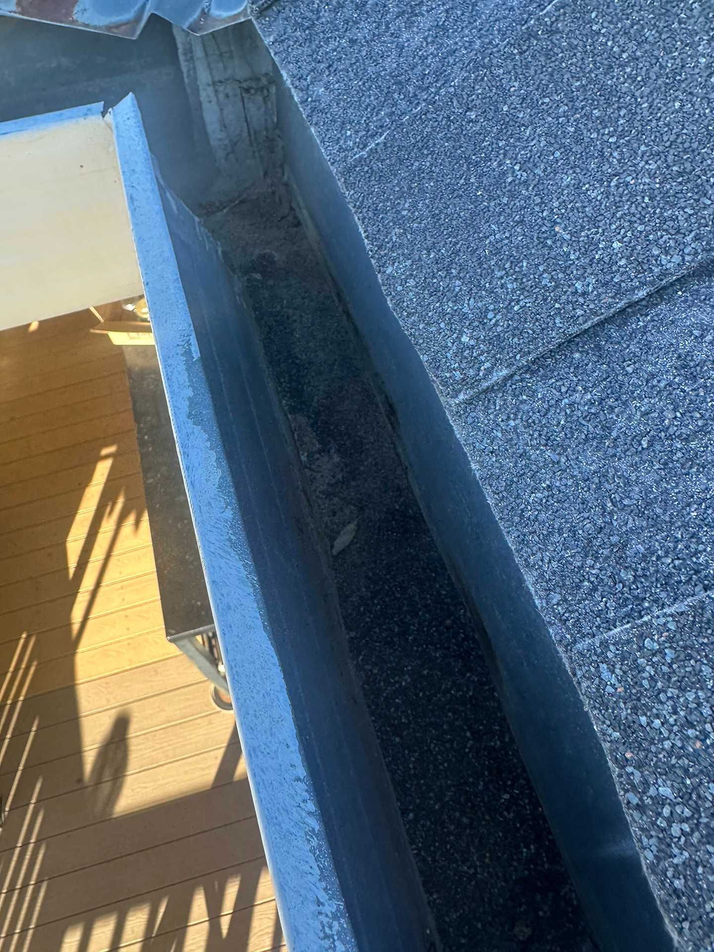 Close-up of a roof edge with shingles, metal flashing, and a dark gutter or drainage channel.