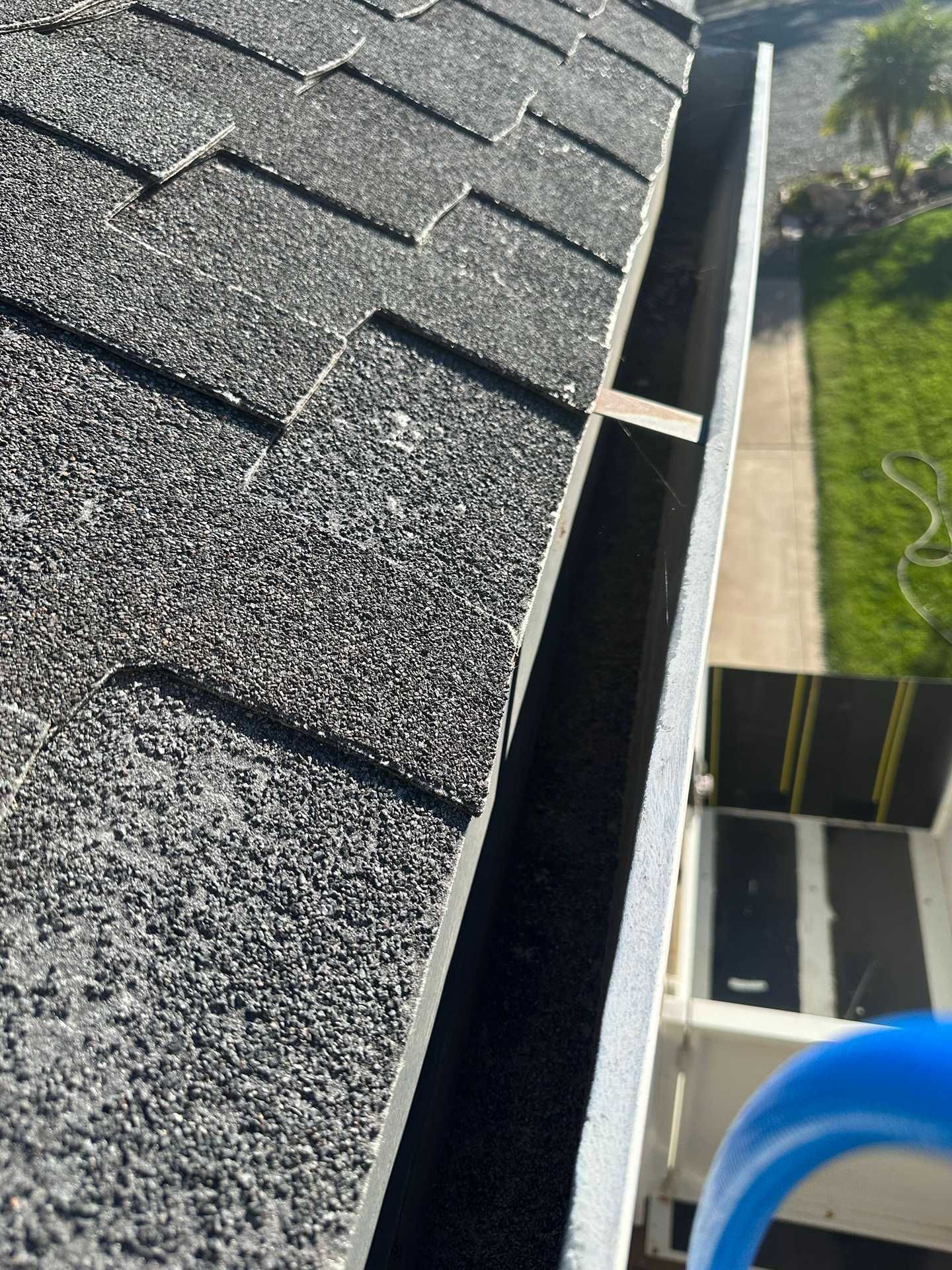 Close-up of gray shingle roof edge with an open gutter and green lawn below