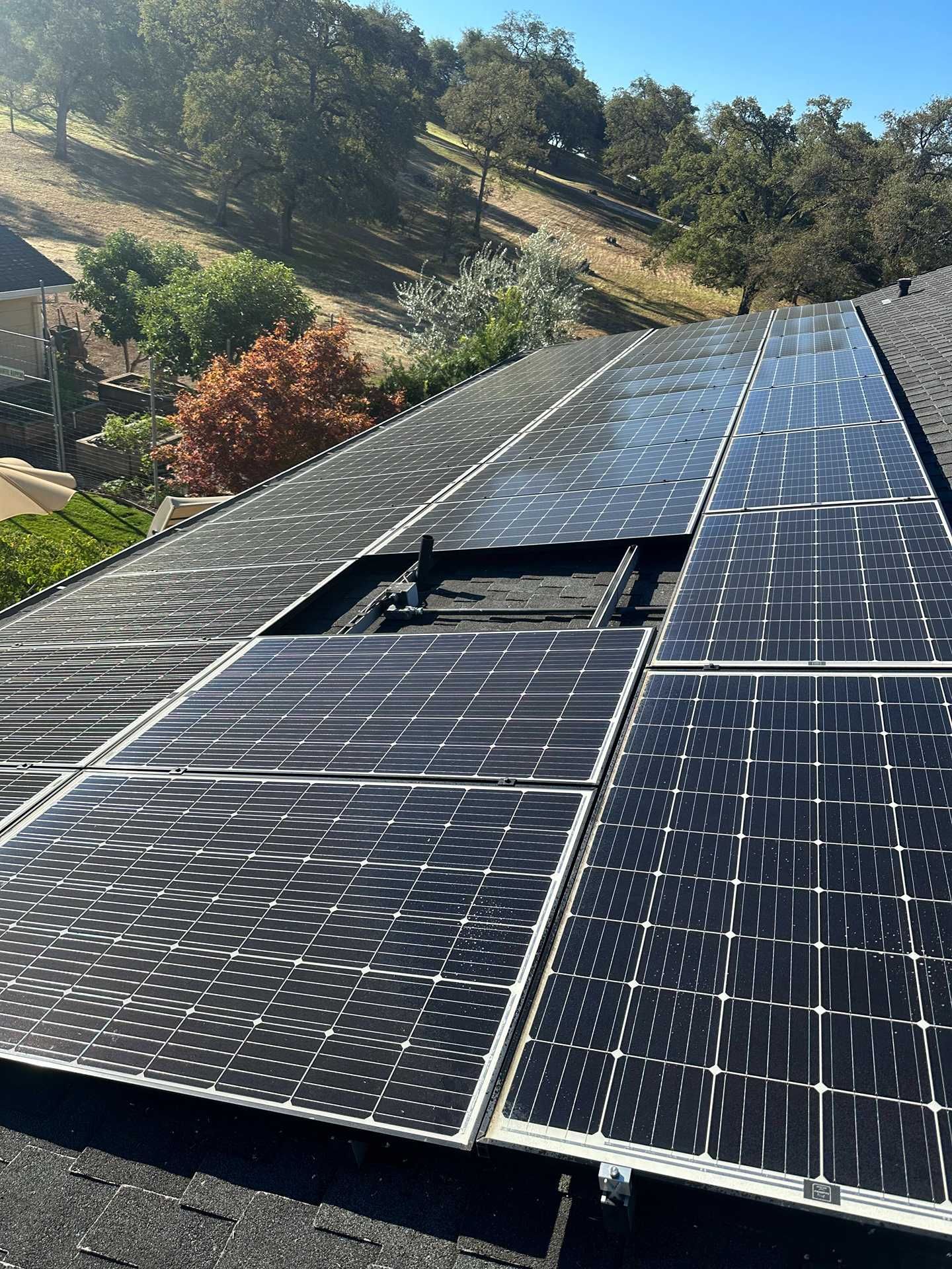 Solar panels on a roof, with one panel damaged or missing, overlooking a wooded hillside.
