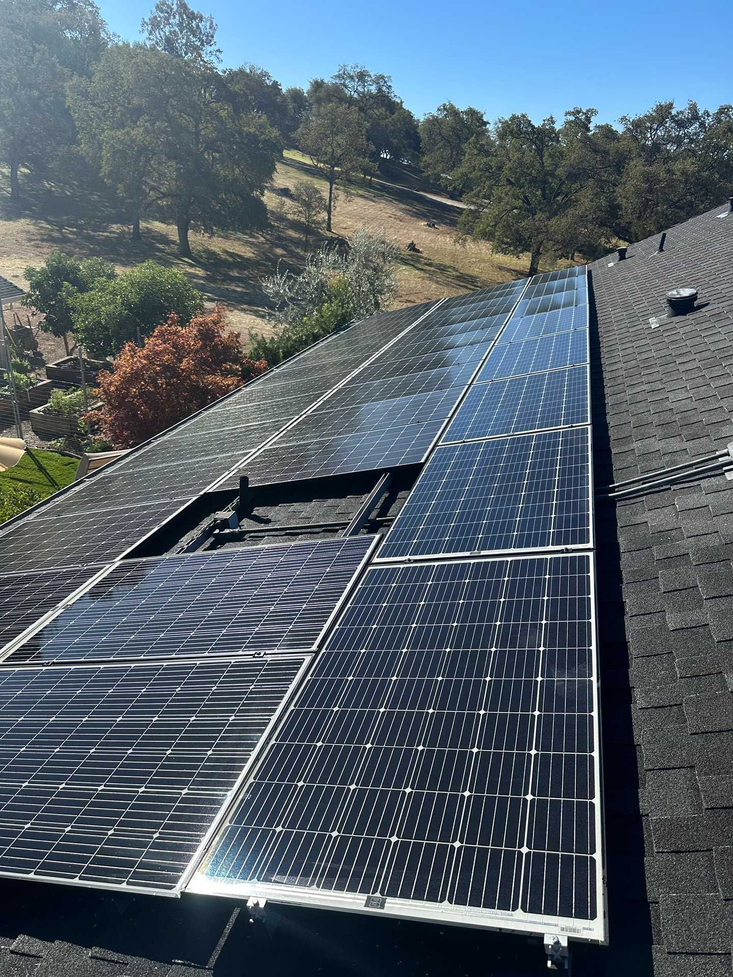 Solar panels installed on a sloped roof with trees and hills in the background.