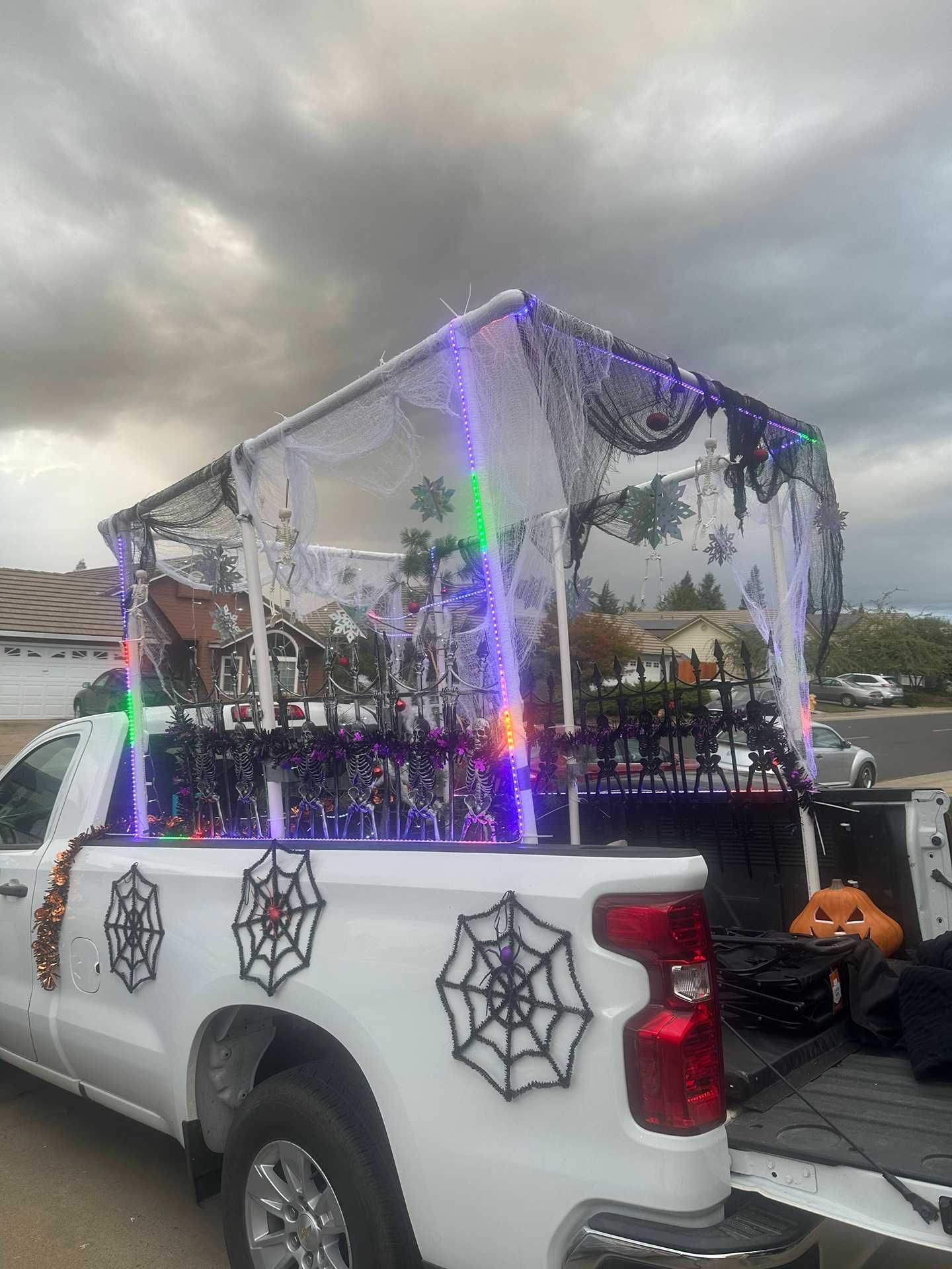 White pickup truck with spiderweb decals and a lit Halloween display in the bed under a cloudy sky
