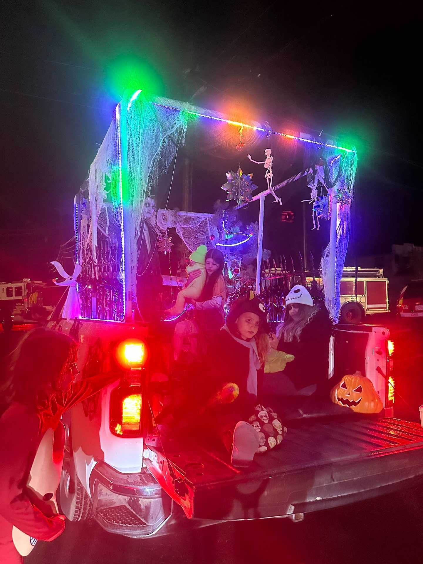 Decorated pickup truck with glowing colorful lights and people riding in the back at night