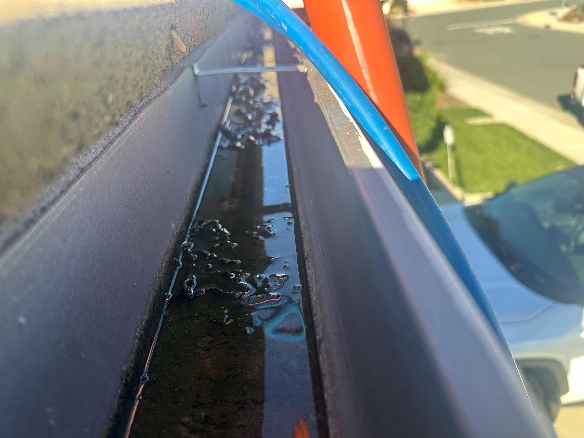Close-up of a wet black gutter beside a house roof, with orange and blue cables running along it