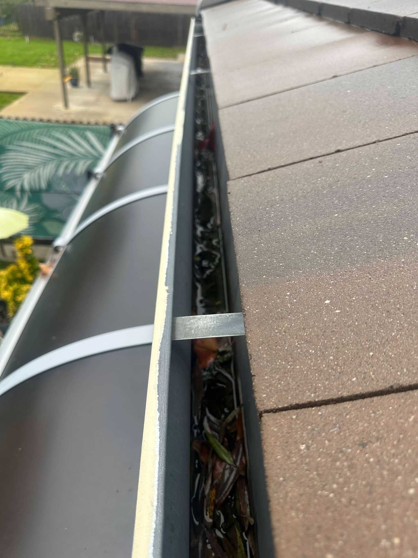 Clogged roof gutter beside brown shingles, filled with leaves and debris