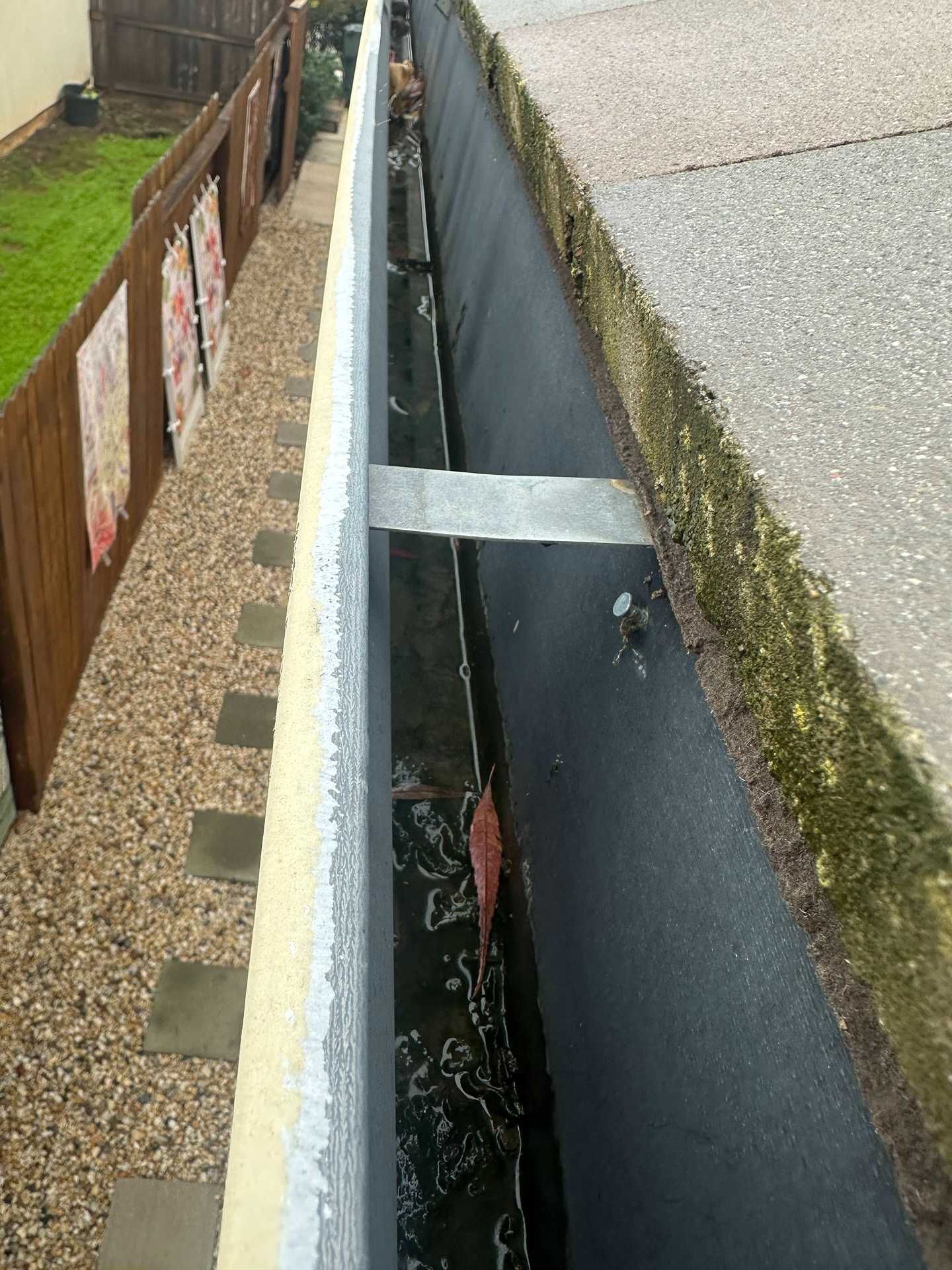 Open roadside drainage gap beside sidewalk and fence, with water below and metal crossbar.