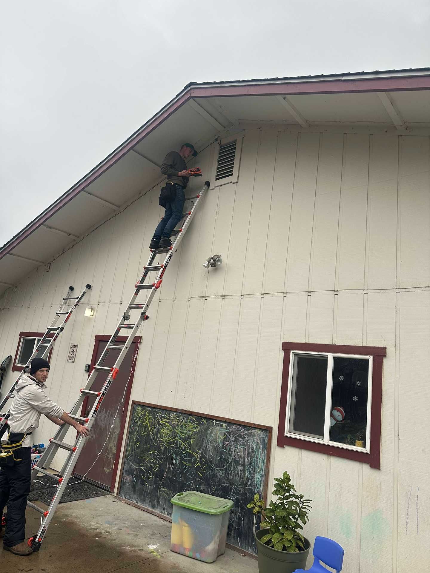 Workers on ladders painting a beige barn exterior near the roof.