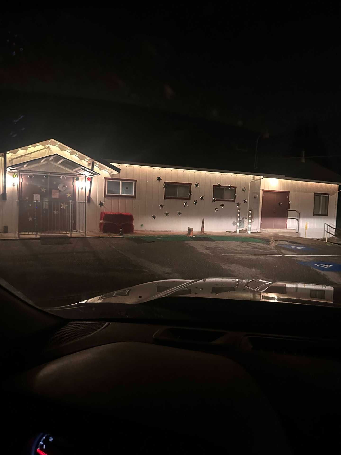 Nighttime view of a small lit motel or office building from inside a parked car
