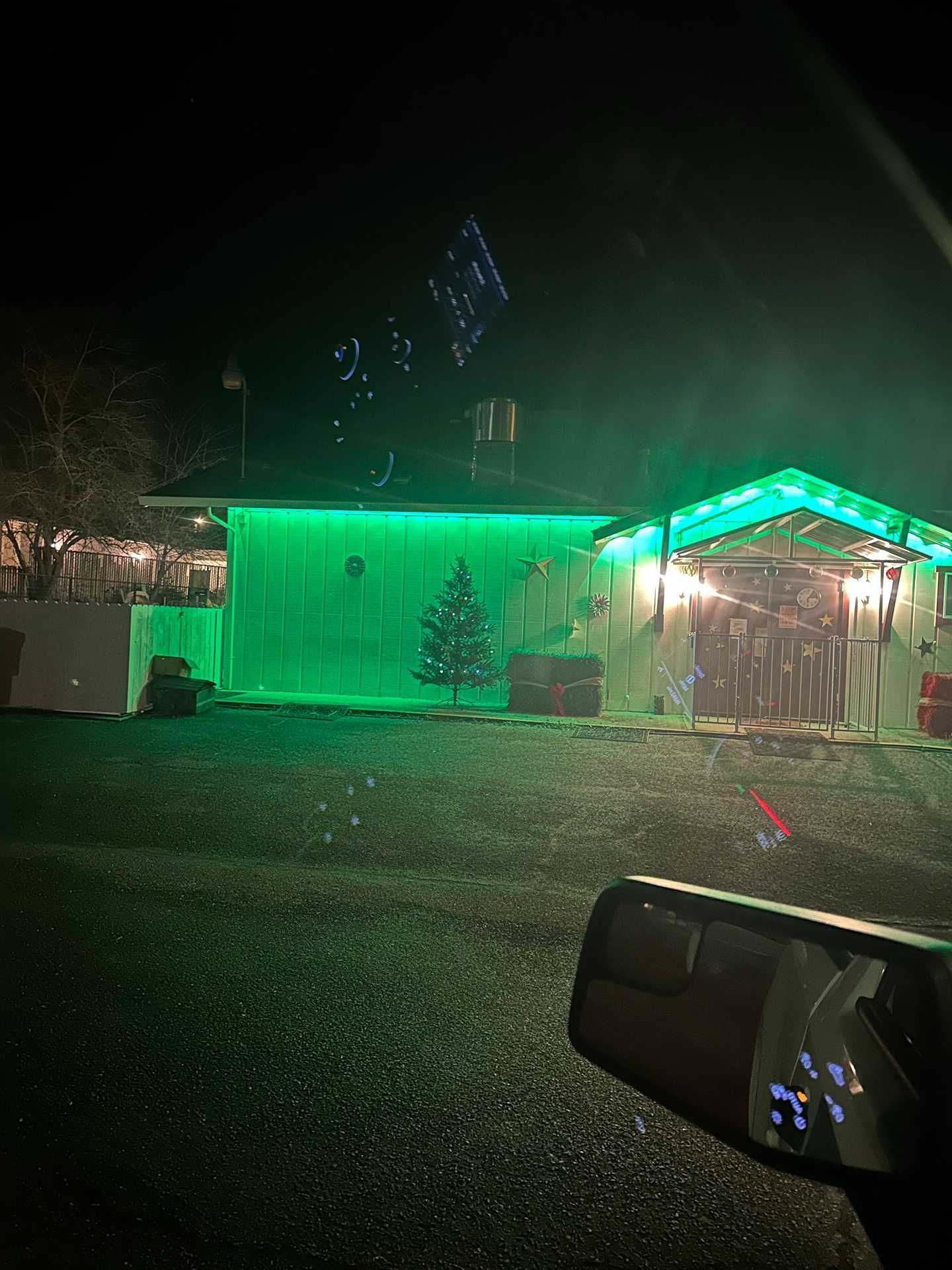 House decorated with green Christmas lights at night, with a lit garage and snow on the ground.