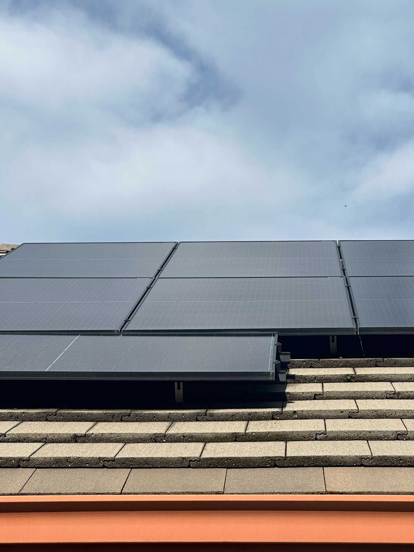 Solar panels mounted on a tiled roof beneath a cloudy sky