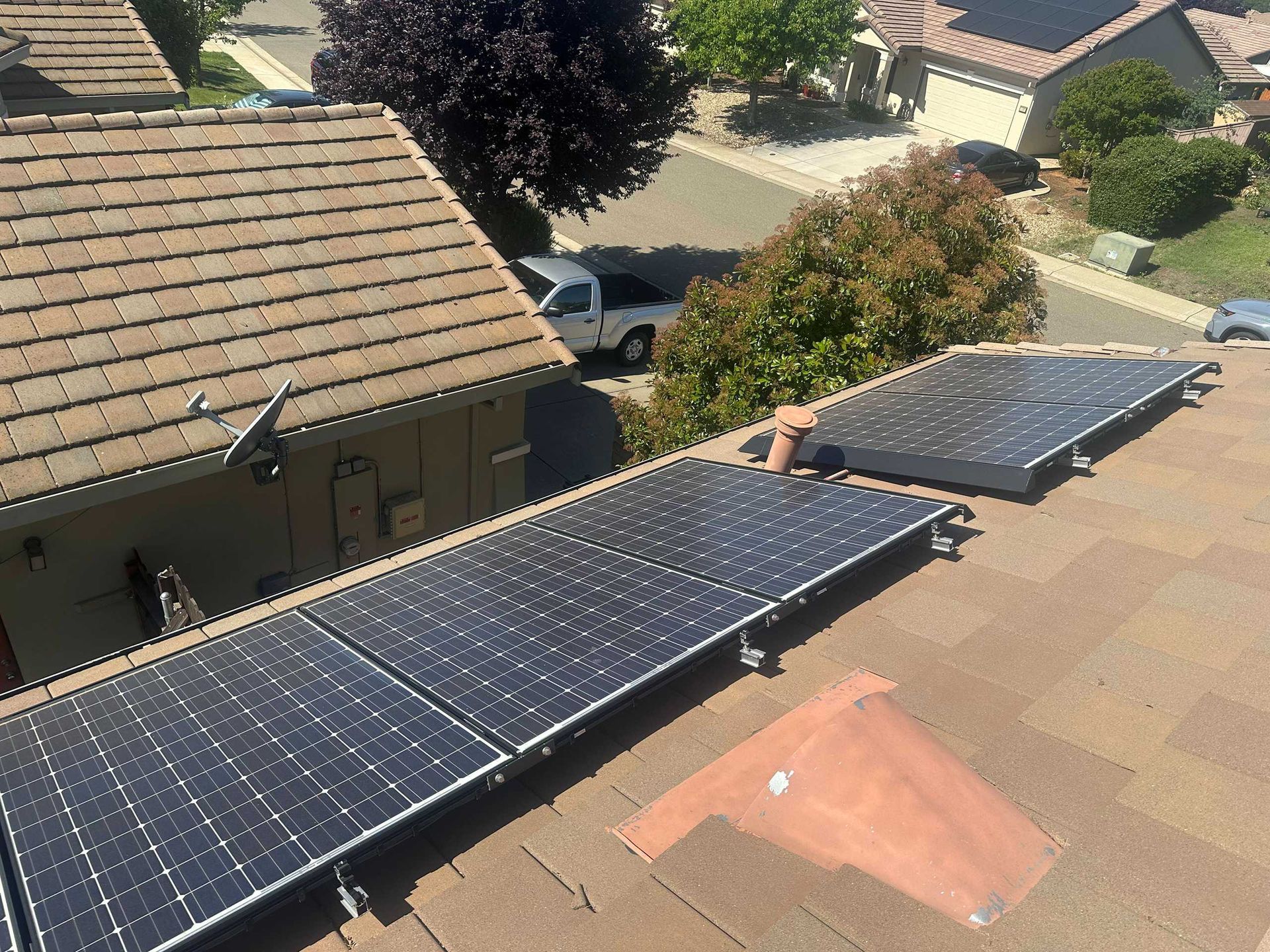 Solar panels mounted on a sloped rooftop beside neighboring houses and trees