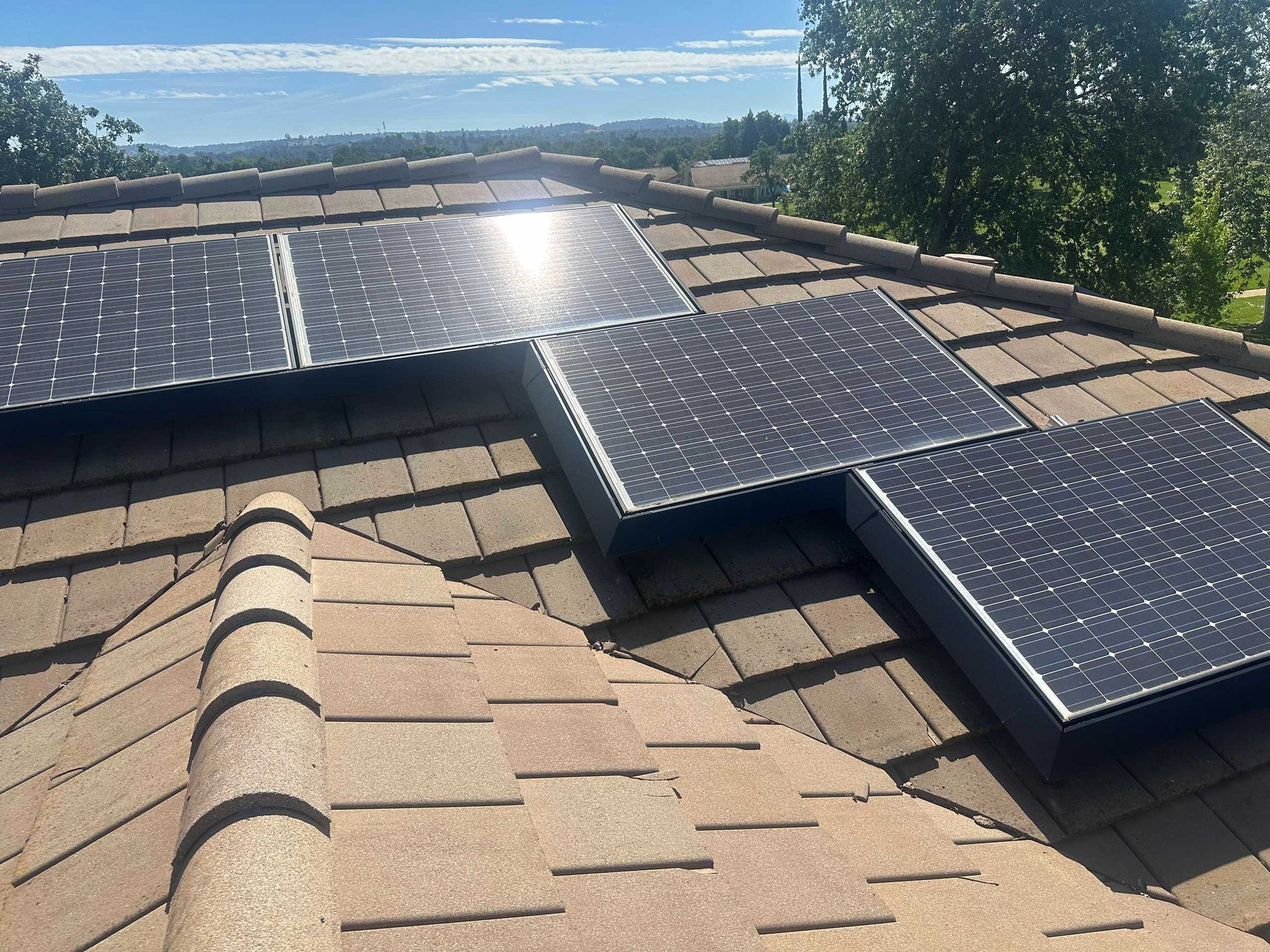 Solar panels installed on a tan shingle roof with hills and sky in the background