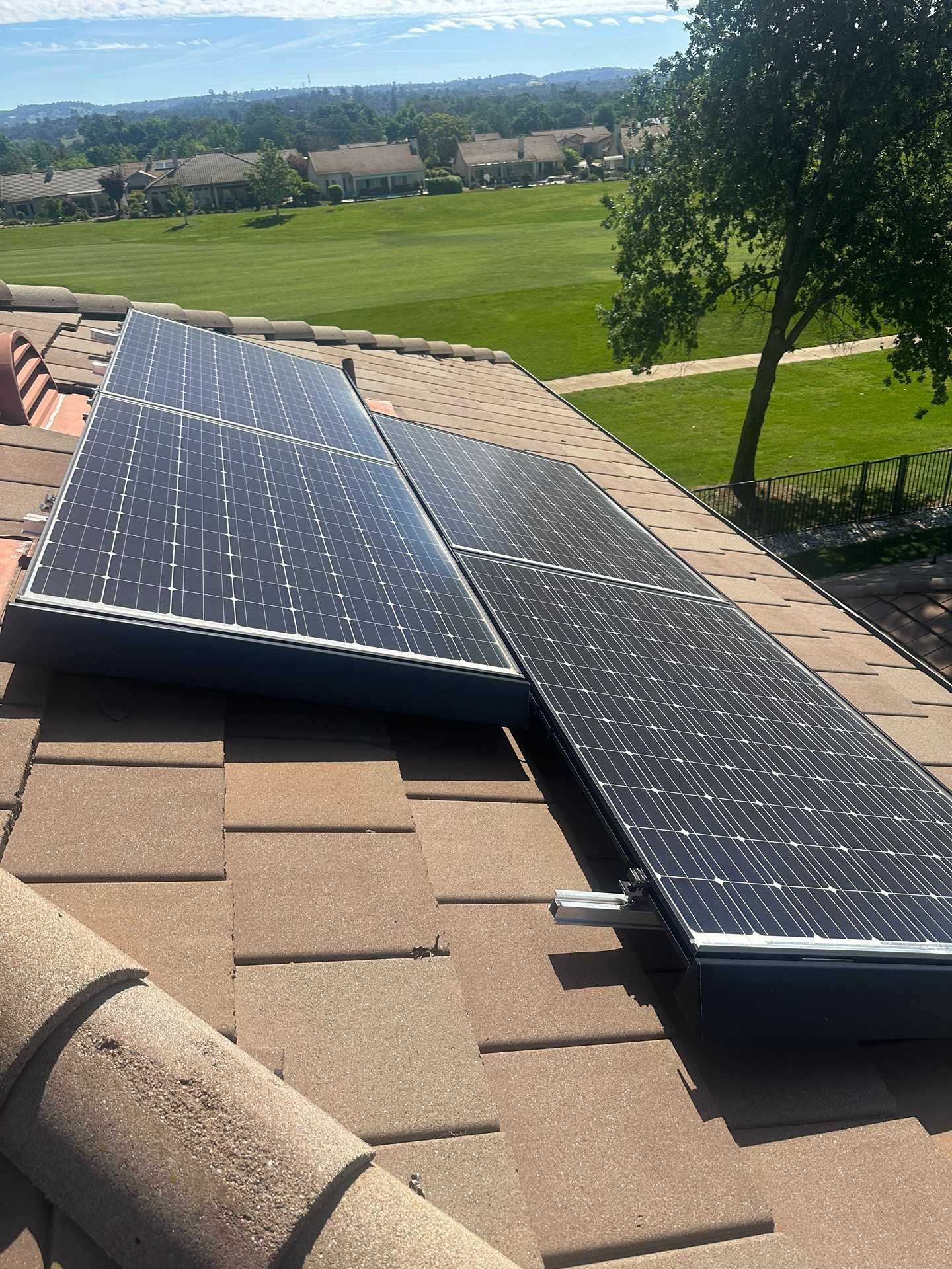 Solar panels installed on a tan shingle roof overlooking a green field and distant hills