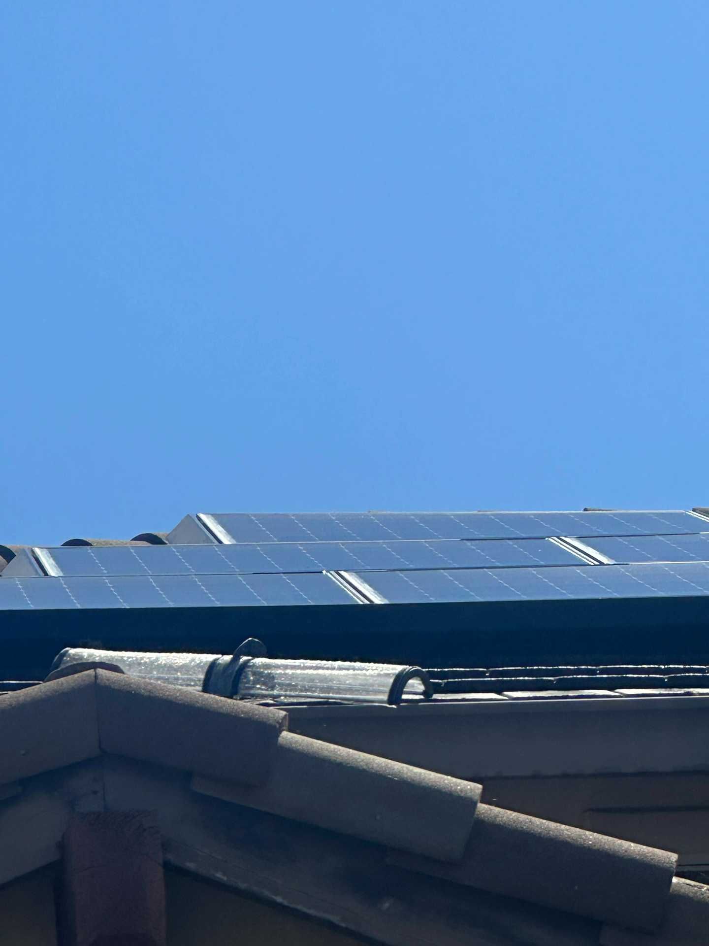 Rooftop solar panels under a clear blue sky, viewed above a house roof.