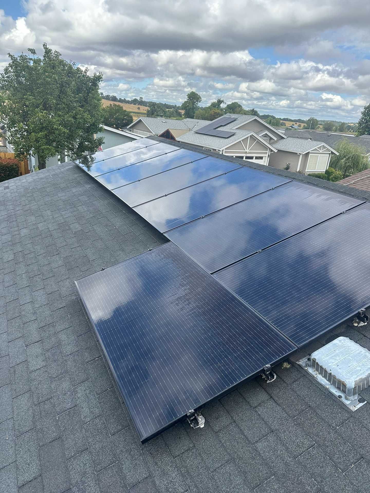 Solar panels mounted on a gray shingled rooftop under a cloudy sky
