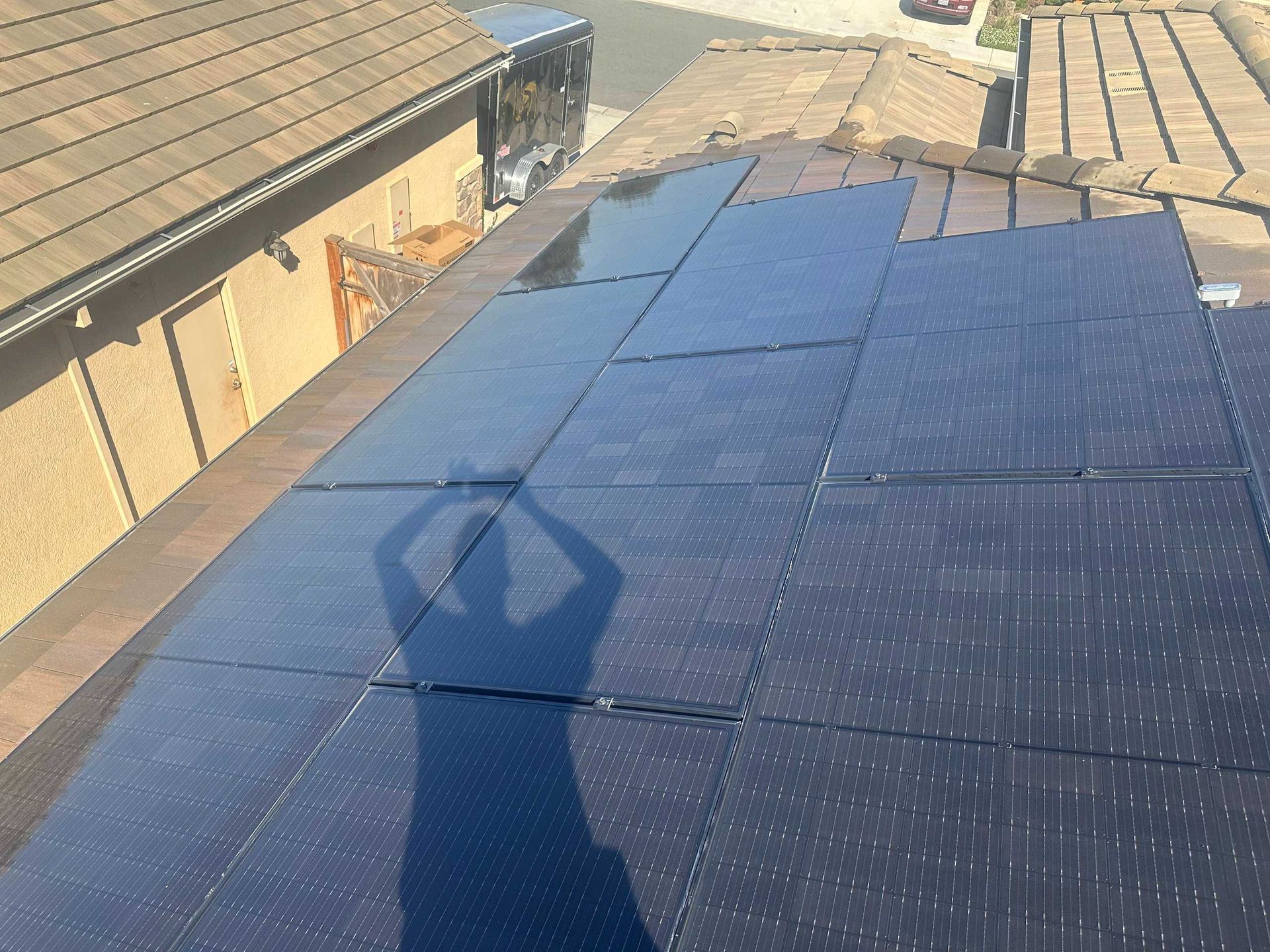 Solar panels on a rooftop beside a house, with a person’s shadow in the foreground.