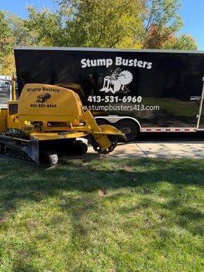 A yellow stump grinder next to a black trailer with the