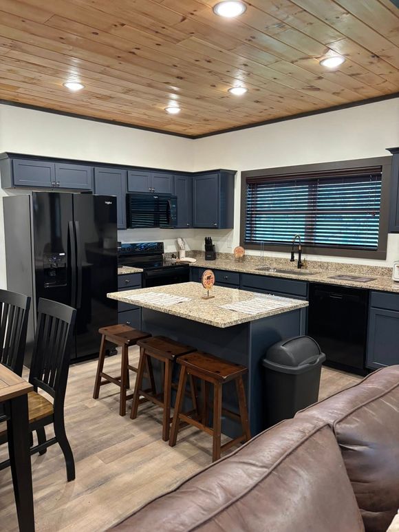 Modern kitchen with dark cabinets, granite island, stainless appliances, and window blinds