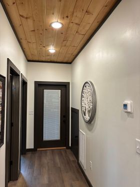 Narrow hallway with wood ceiling, dark floors, white walls, doors, and wall decor.
