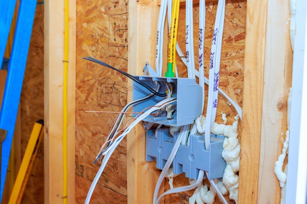 Electrical wiring in an unfinished wall with open junction box, cables, and spray foam insulation