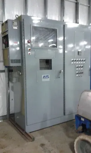 Large gray industrial machine cabinet with a window, buttons, and control panel inside a warehouse