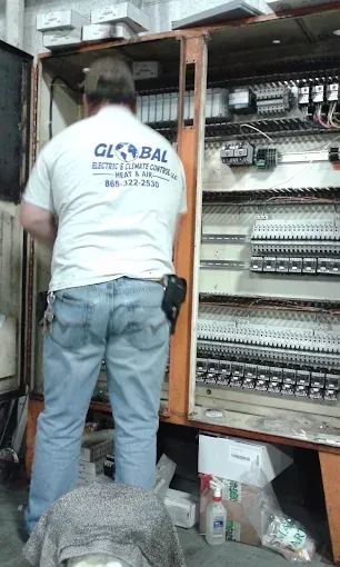 Technician working inside an open electrical panel, wiring and circuit breakers visible.