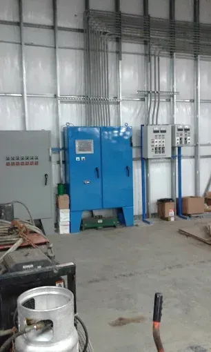Blue industrial machine against a warehouse wall with electrical panels and scattered tools on a concrete floor