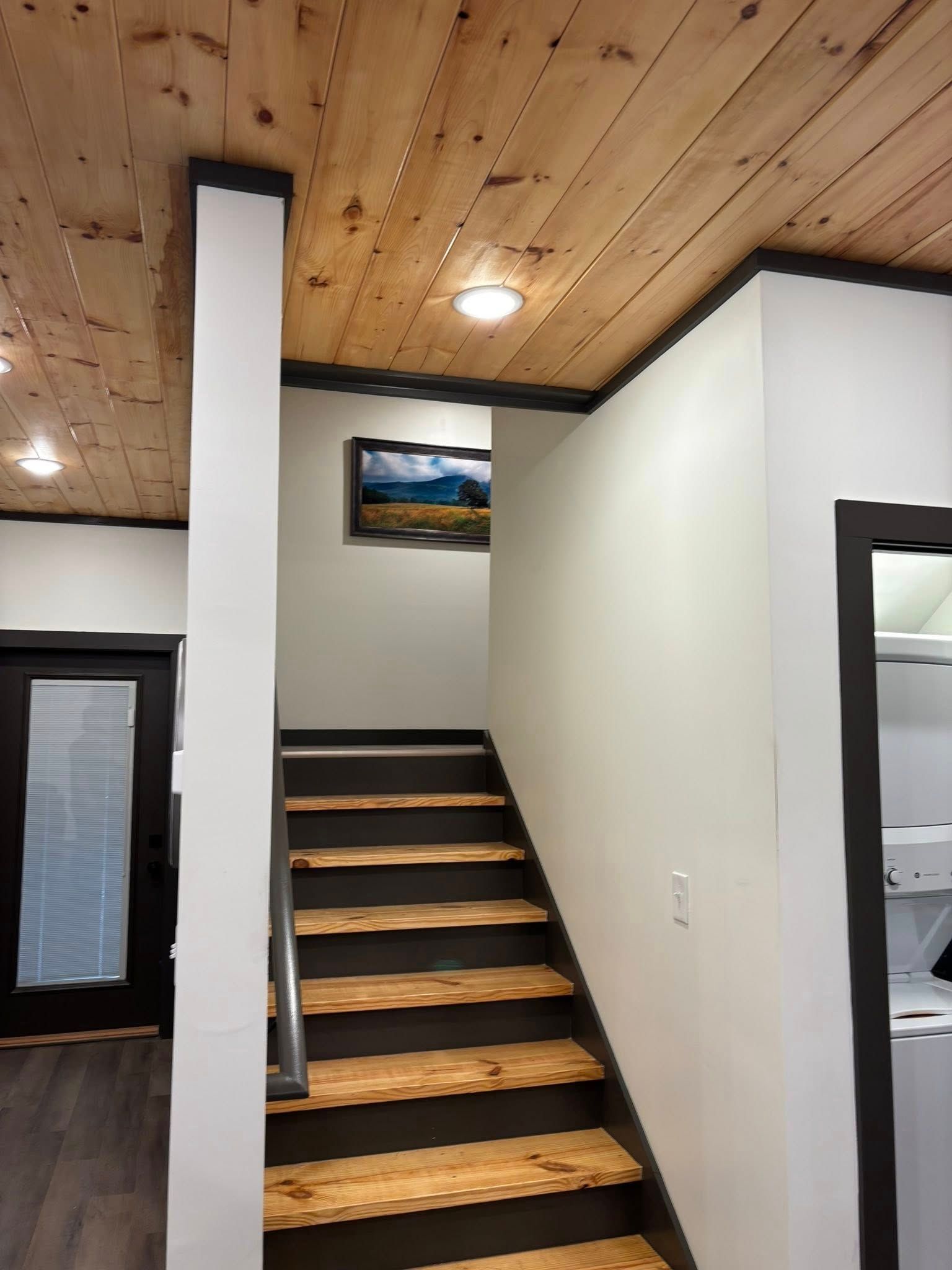 Interior stairway with wood ceiling, black rail trim, and framed landscape art above the steps