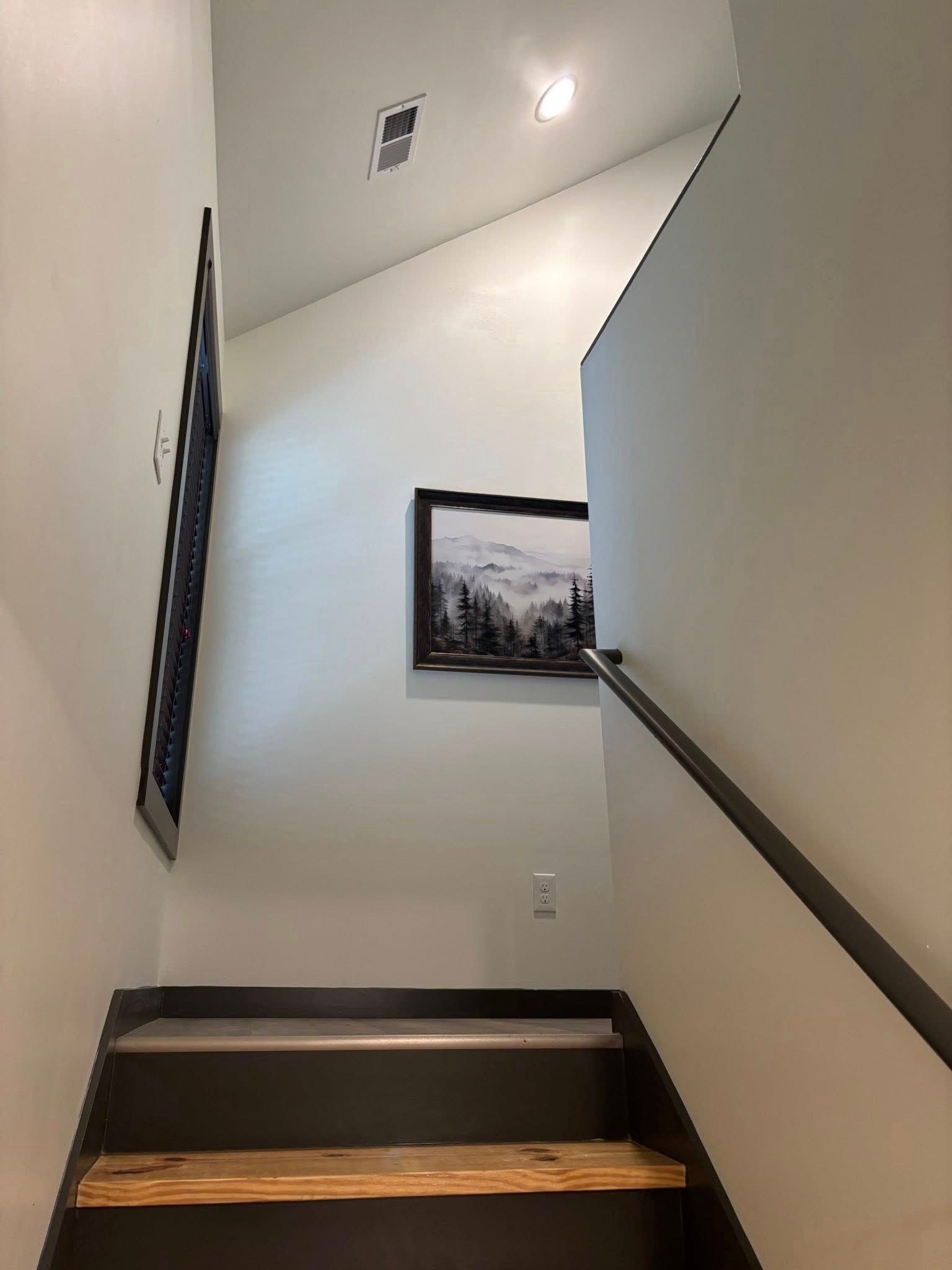 Stairwell with white walls, dark railings, and framed artwork on the landing.