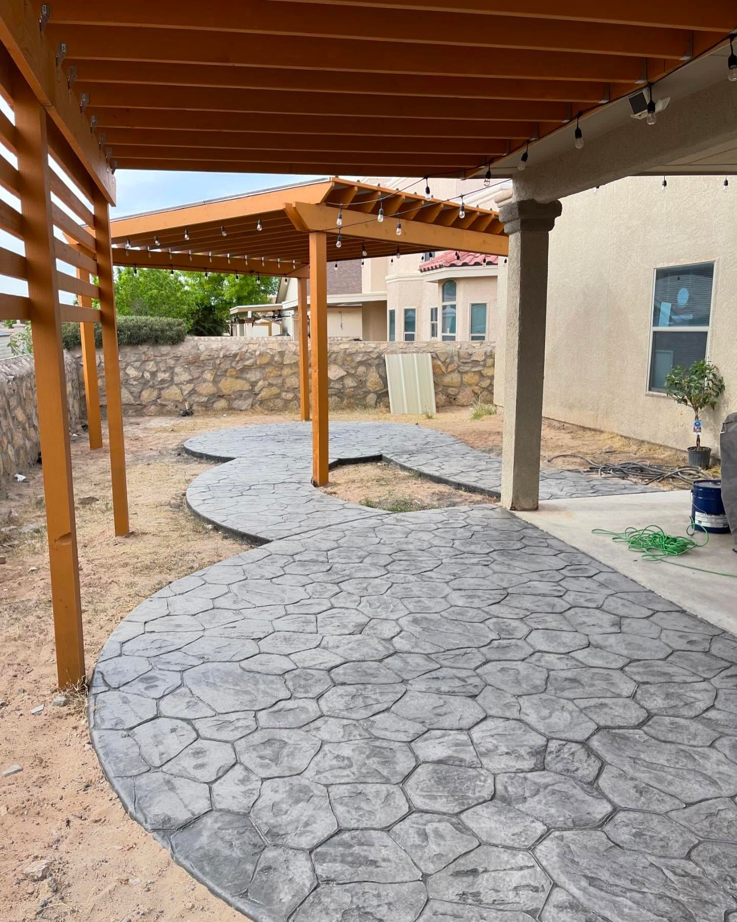 Covered outdoor walkway with stamped concrete path, wooden pergola, and stone wall in a courtyard