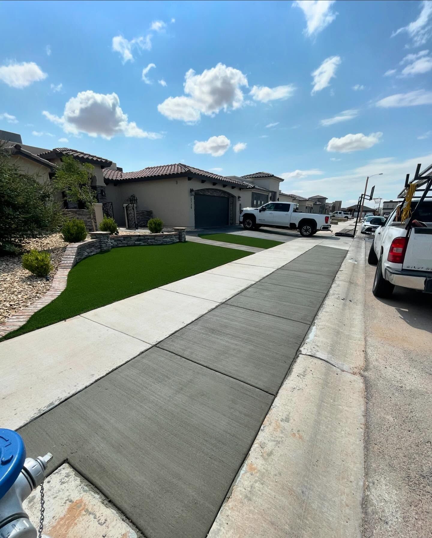 New concrete driveway beside a house, with a white truck parked on a sunny residential street.