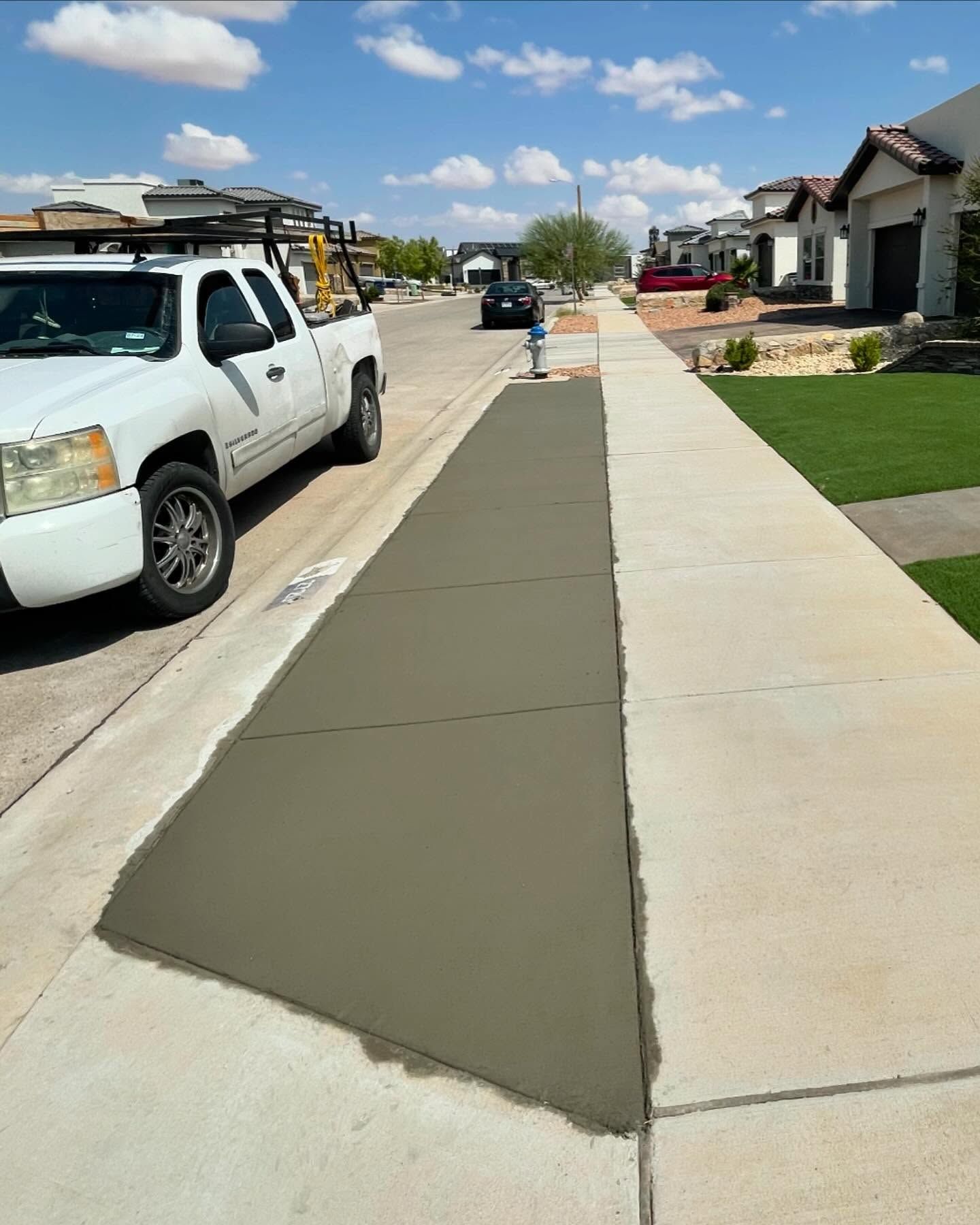 Sidewalk with fresh dark concrete repair beside a residential street and parked white work truck