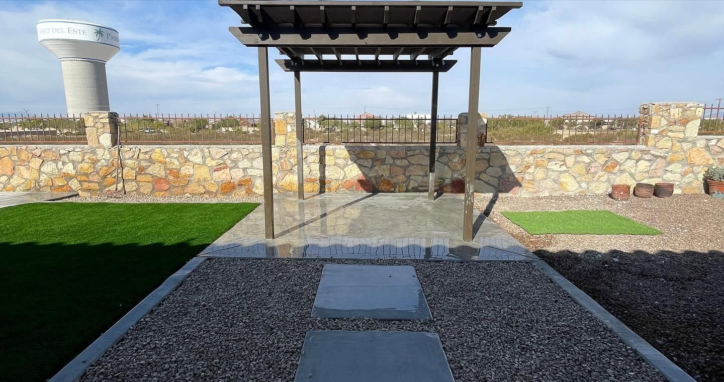 Stone pathway leading to a shaded pergola and benches in a landscaped outdoor garden under clear sky