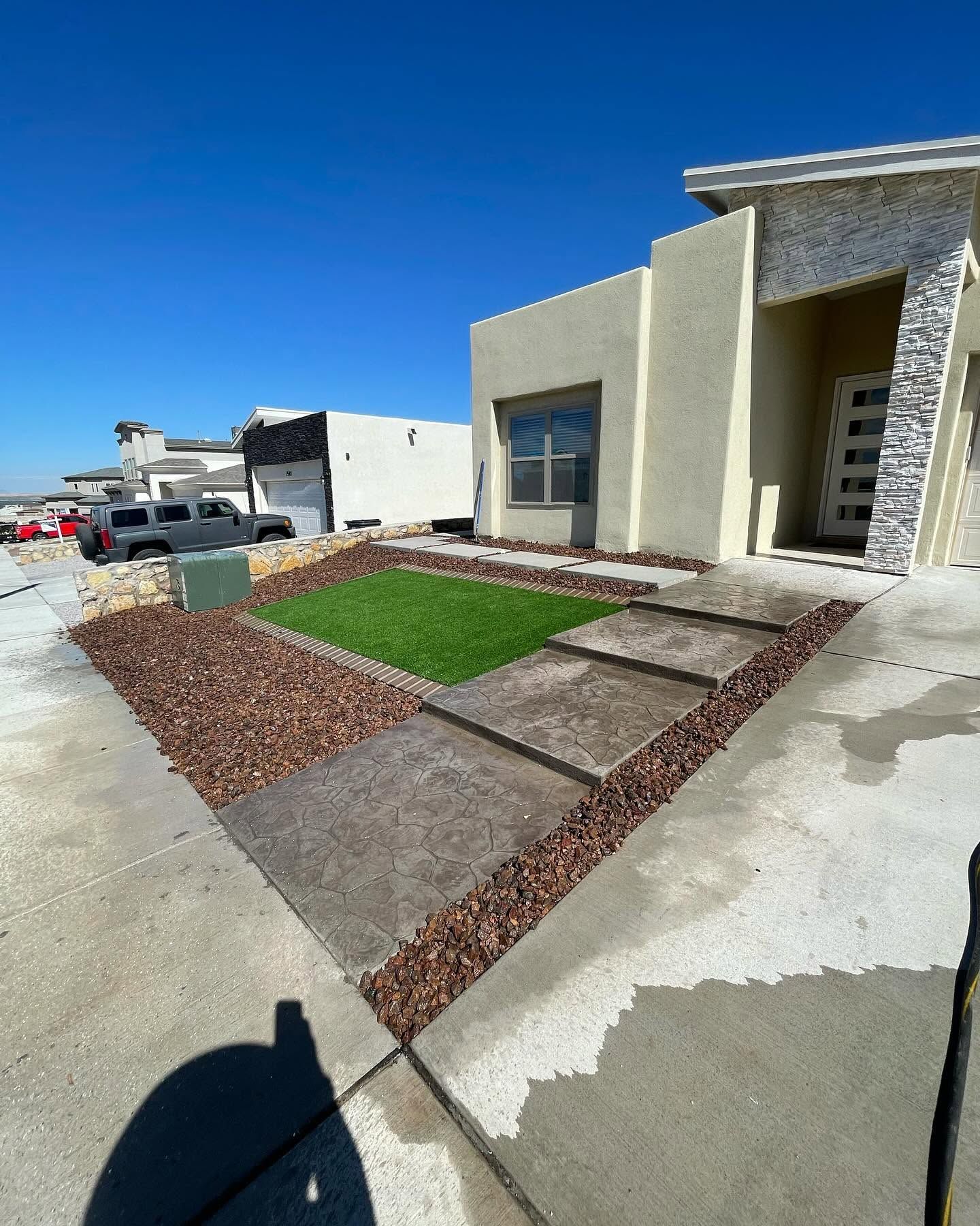 Modern house exterior with a small landscaped courtyard, stone walkway, and green grass patch under a blue sky