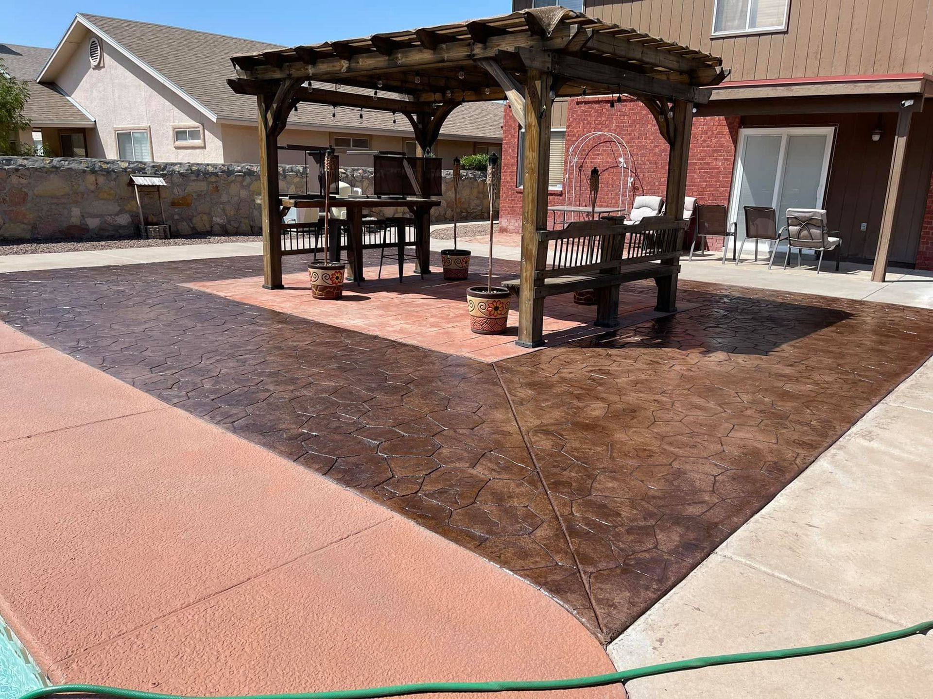 Backyard patio with a wooden pergola, picnic tables, and a brown concrete seating area