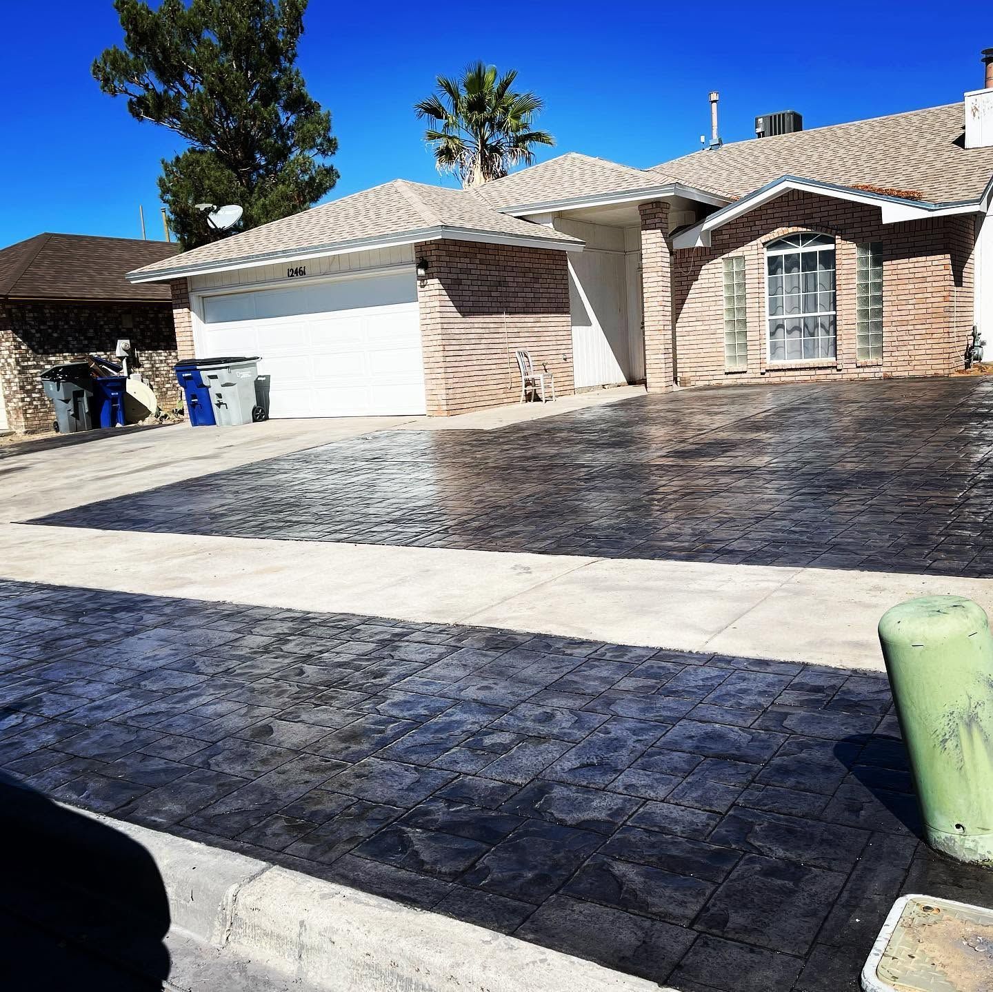Residential driveway with dark stamped concrete and a white garage under a bright blue sky