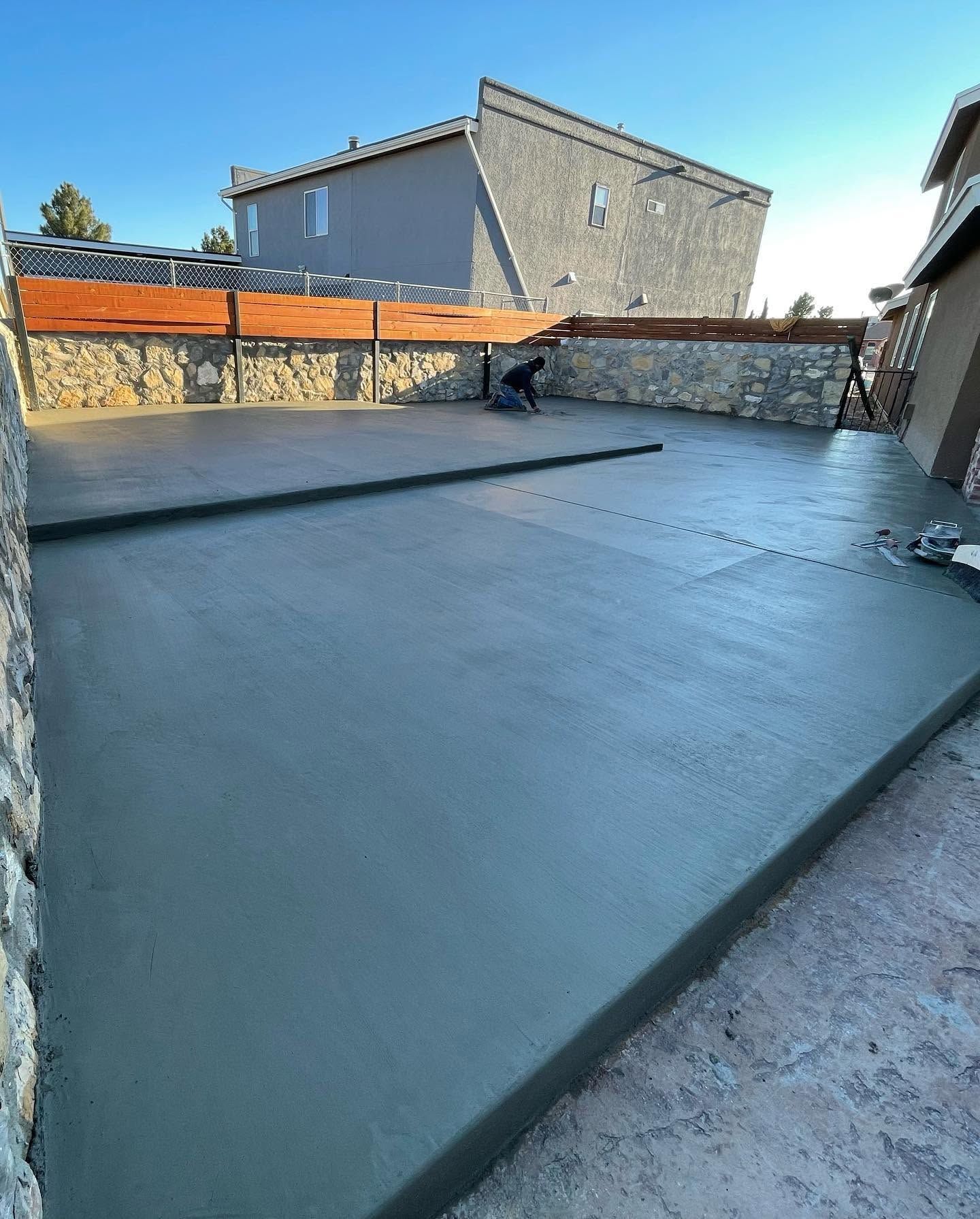 Freshly poured concrete slab in an outdoor courtyard beside stone walls and nearby buildings