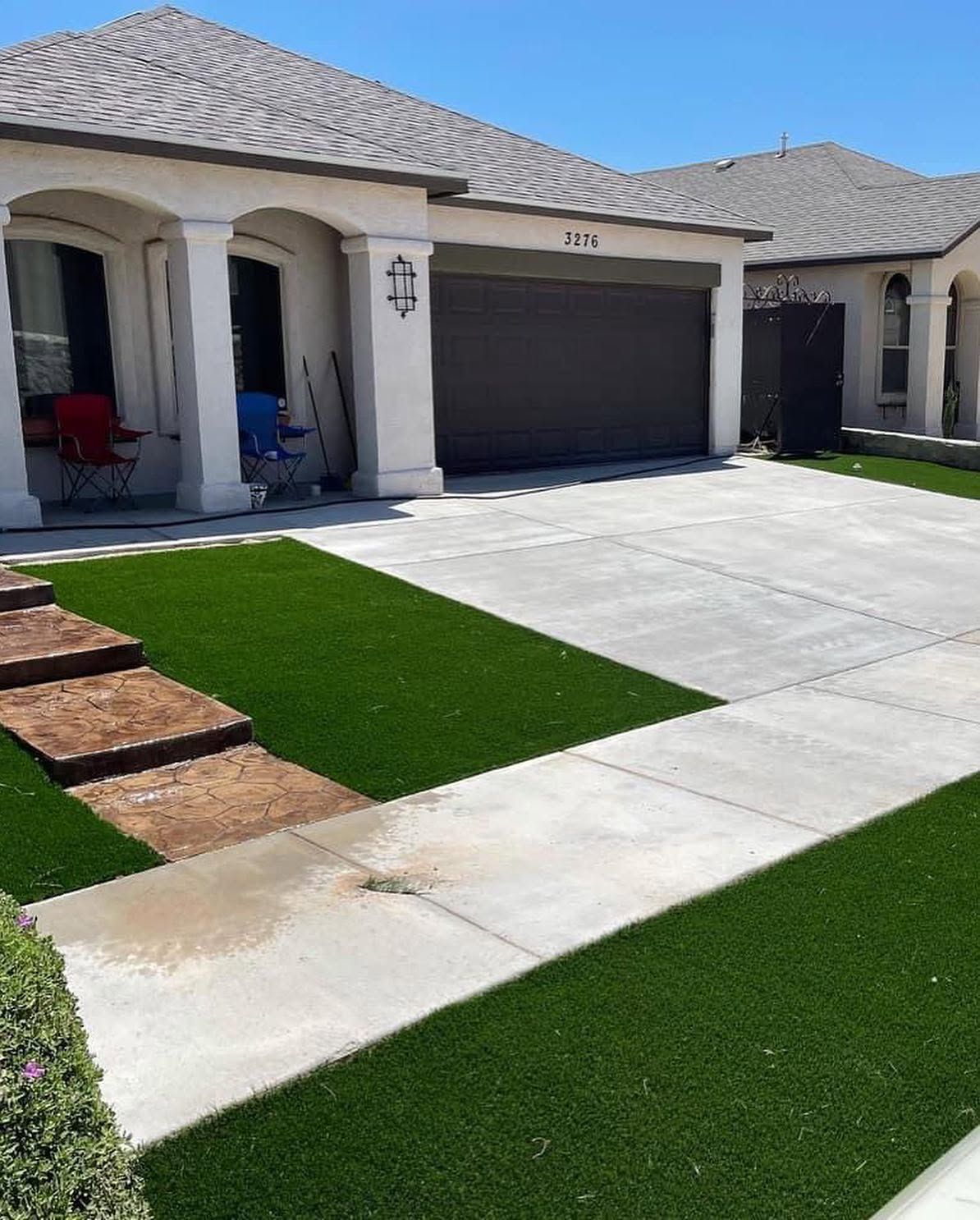 Modern suburban house exterior with a two-car garage, white driveway, and green lawn under a blue sky