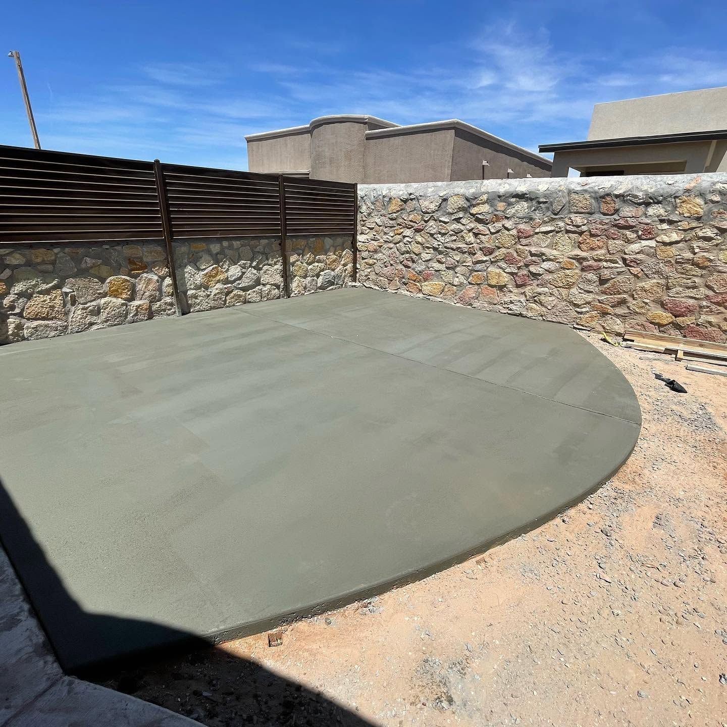 Concrete patio pad in a walled backyard under construction, with stone walls and gravel ground