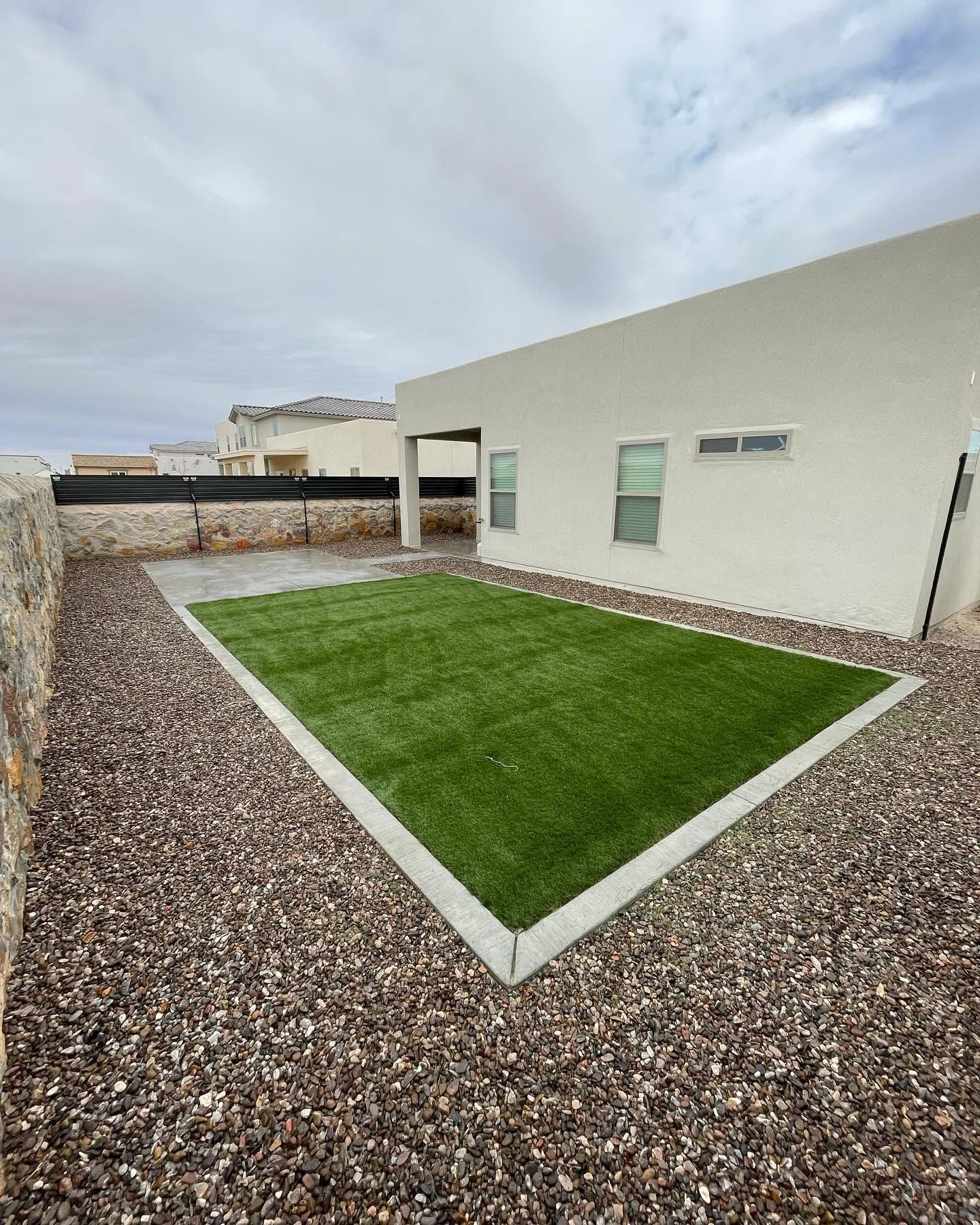 Modern house patio with gravel border and a small rectangular green lawn under a cloudy sky
