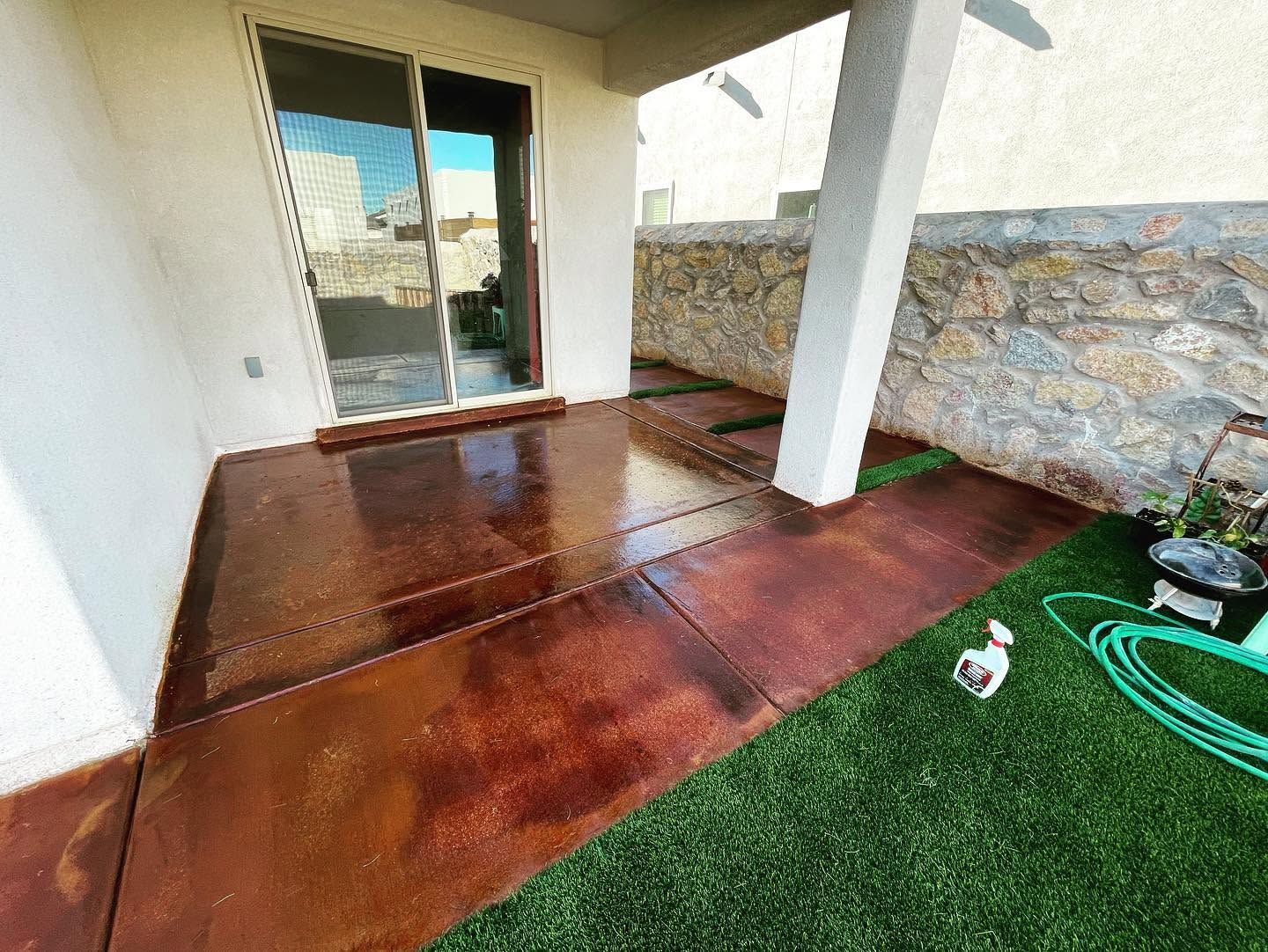 Covered patio with stained concrete floor, stone wall, sliding glass door, and green artificial turf edge
