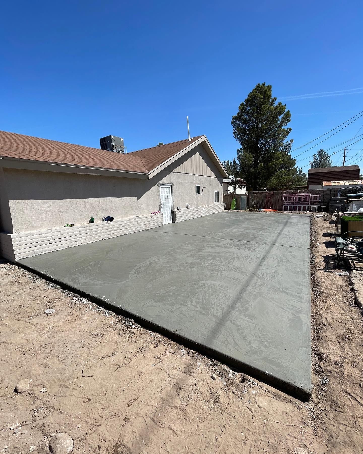 Fresh concrete patio beside a house under a clear blue sky.