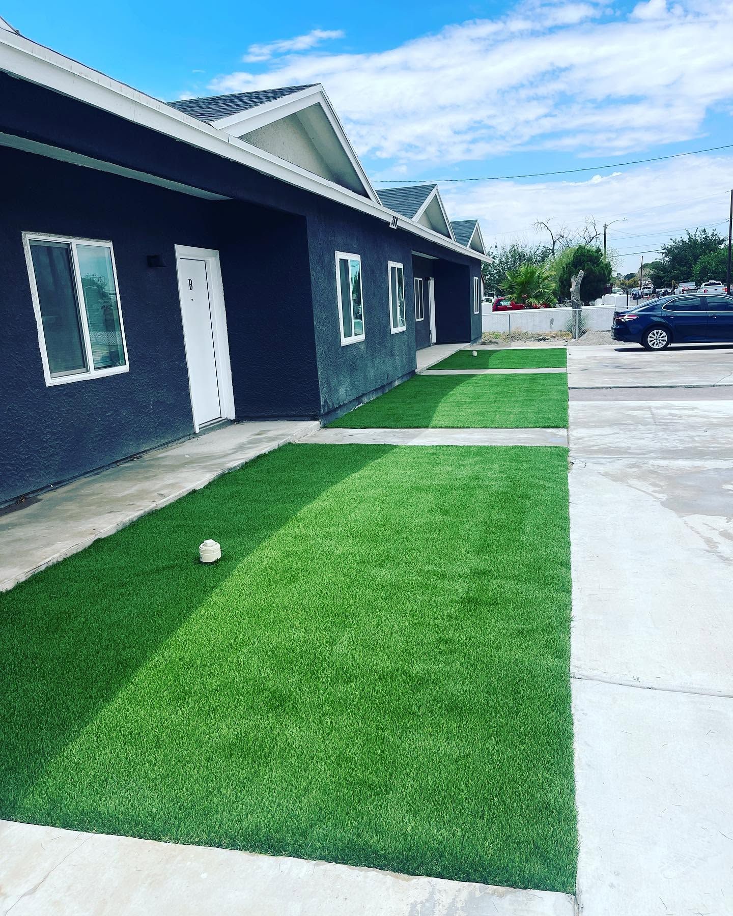 Modern dark house with white doors, green lawn strips, and a parking area under a blue sky.